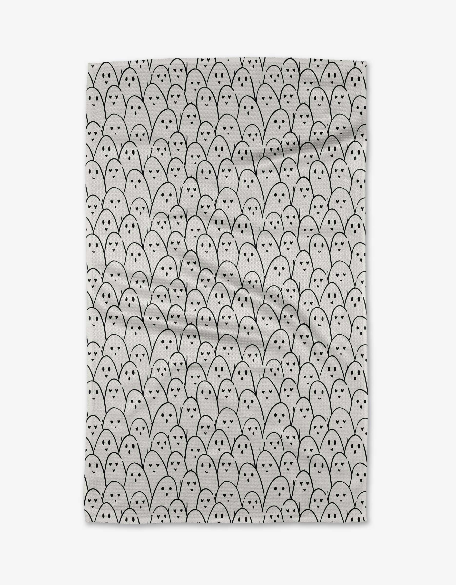 The Happy Ghosts tea towel by Hufton Studio features a close-knit pattern of black and white cartoon ghost faces on a light background, each with round eyes and an oval mouth. Crafted from recycled materials.