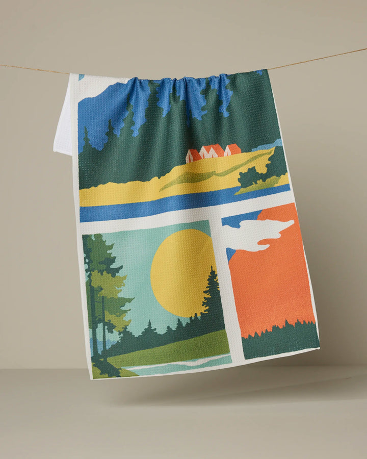 The Geometry "Happy Hiking" tea towel features vibrant nature-inspired graphics—trees, sun, mountains, and red houses—set on a beige background. Made from recycled materials, it adds color and eco-friendly style to your kitchen décor.
