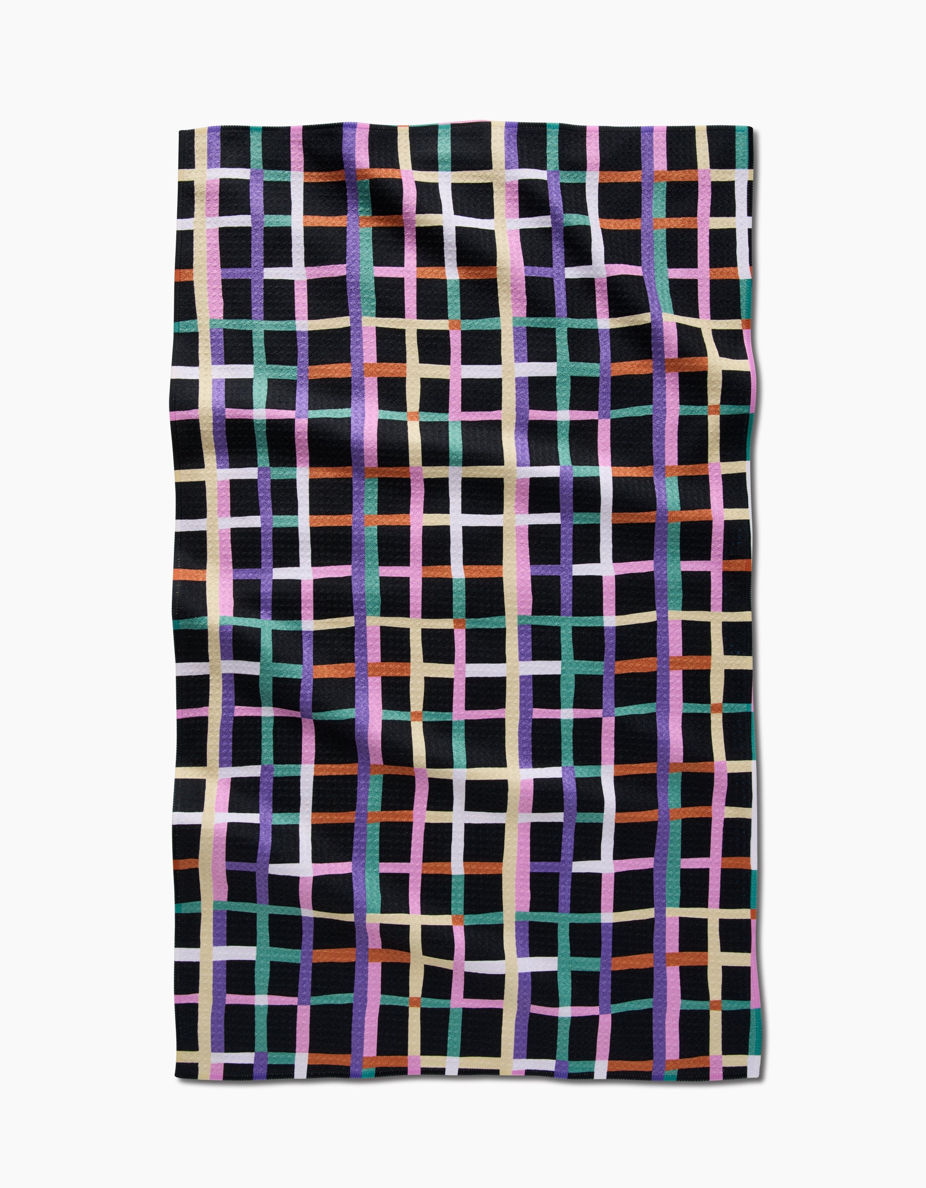 A slightly wrinkled Claire Iglesias Happy Plaid tea towel, made of textured Geoweave™ fabric with intersecting purple, mint green, orange, white, and pink grid lines on black, is laid flat on a white surface.