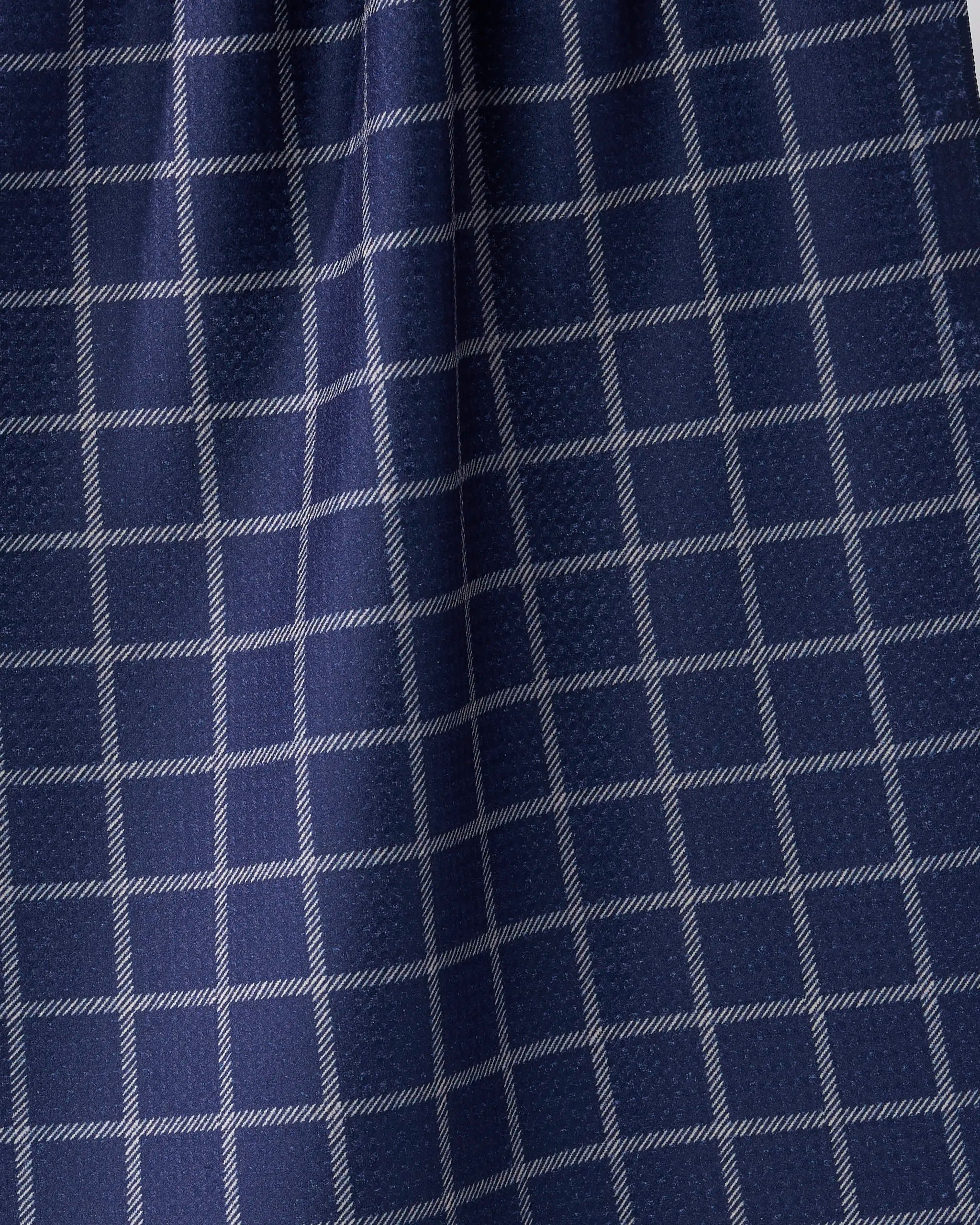 A close-up of Geometry’s Harbor Plaid shows dark blue fabric with a white grid, reminiscent of classic tea towels. Gentle folds add depth to the geometric pattern—perfect for an ultra-absorbent kitchen towel made from recycled materials.