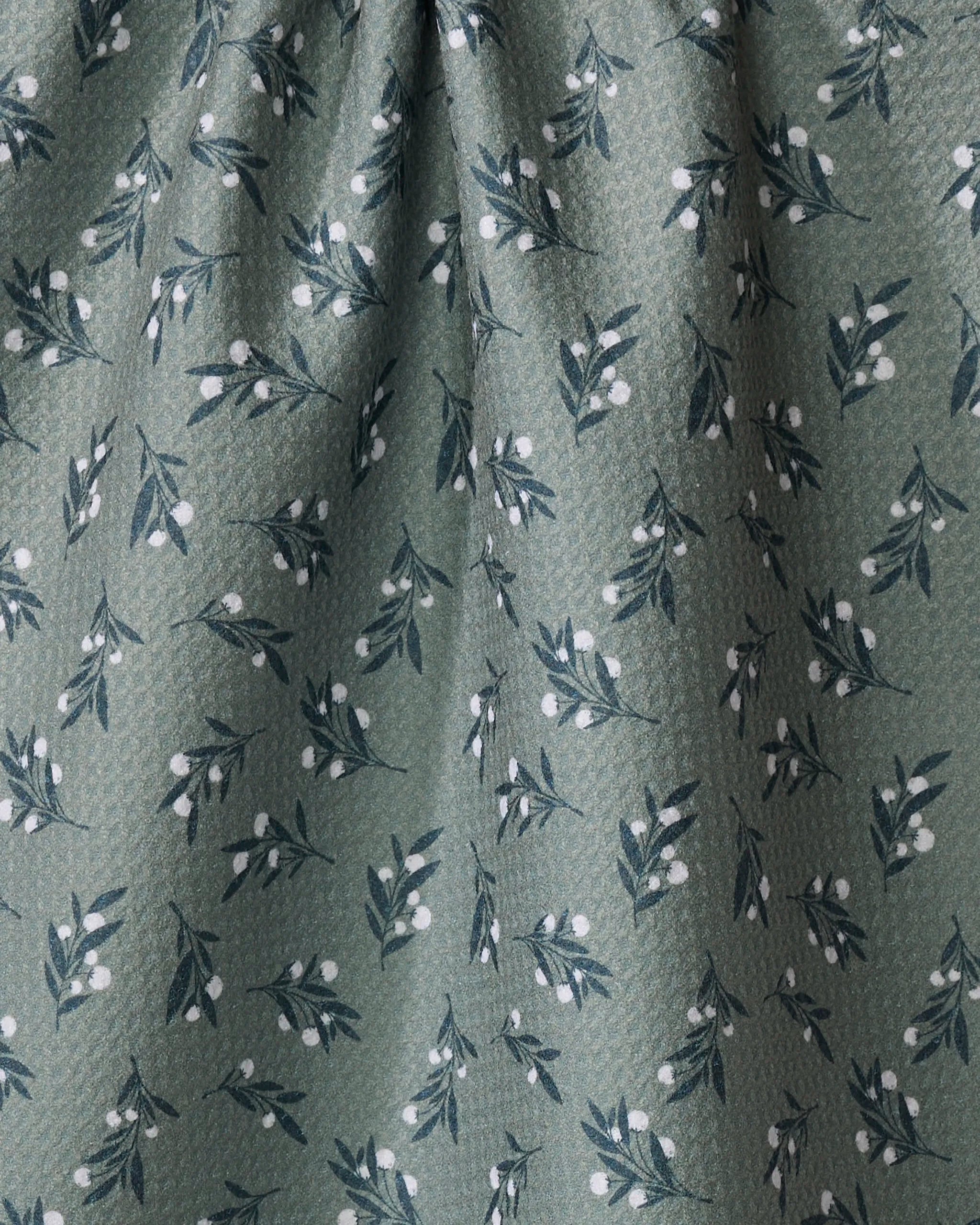 The Harvest Berries dish towel by Charlie Rowan Designs features green fabric with a subtle texture and an absorbent surface, decorated with small dark green leafy branches and white berry clusters.