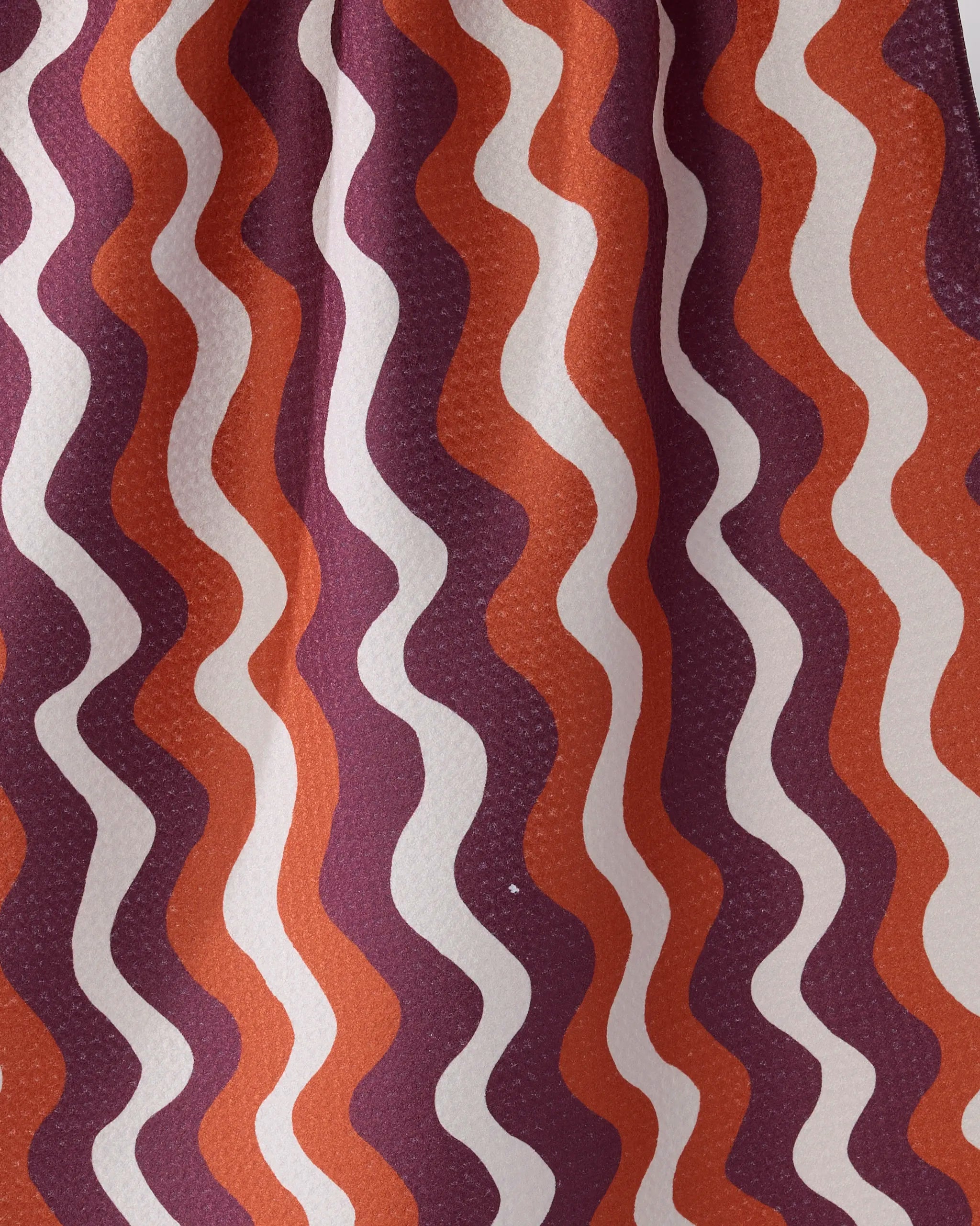 The Harvest Groove tea towel by Geometry features vertically repeating wavy stripes in orange, burgundy, and off-white. Made from recycled materials, its retro design adds vintage flair to your kitchen.