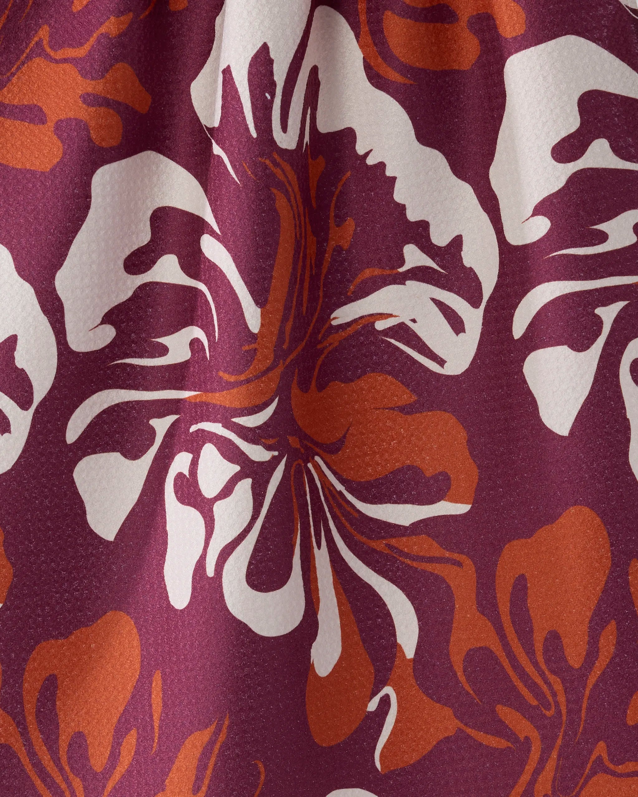 Close-up of Geometry's Harvest Muse tea towel, showcasing a maroon background with bold white and orange abstract floral patterns. The ultra-absorbent fabric features a textured look for effective drying.