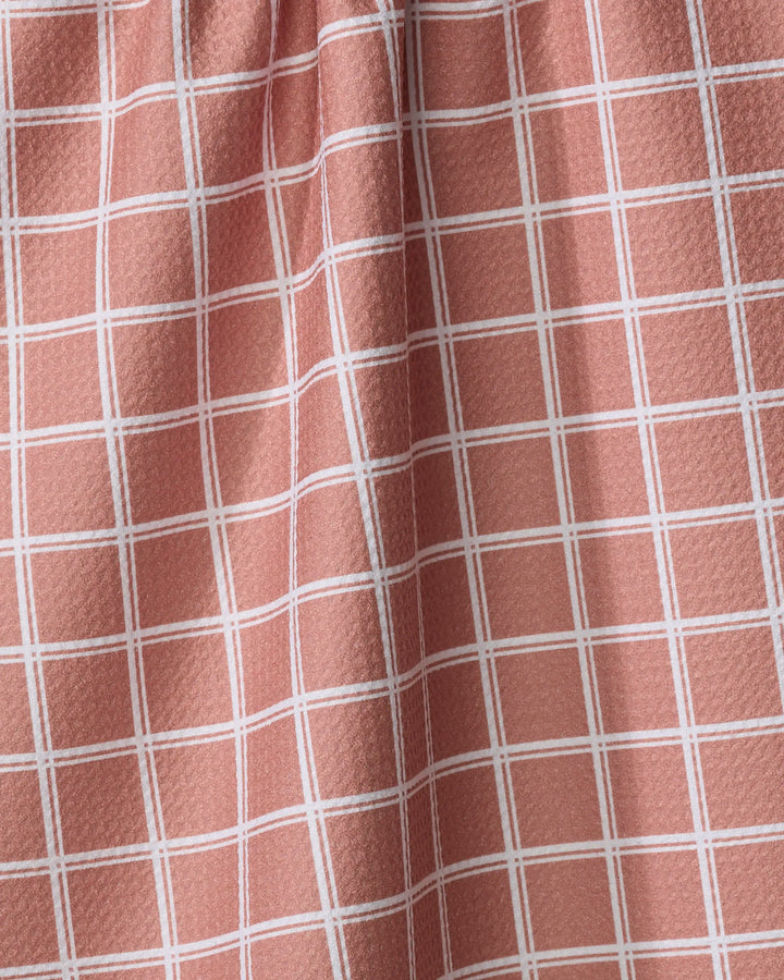 A close-up of the Harvest Plaid tea towel by Charlie Rowan Designs shows its pink and white grid pattern, textured surface, and gentle folds that create subtle shadows and highlights.