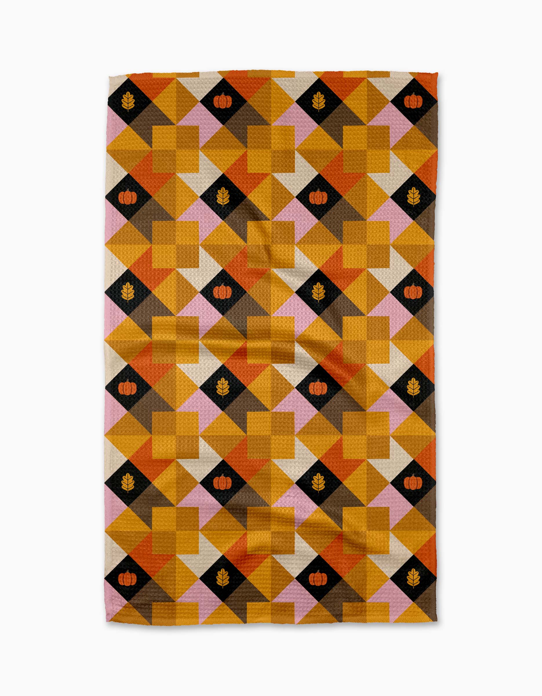 The Harvest Quilt tea towel by Megan Roy features a geometric pattern in autumn hues with pumpkins and leaves on select squares, all crafted from recycled materials.
