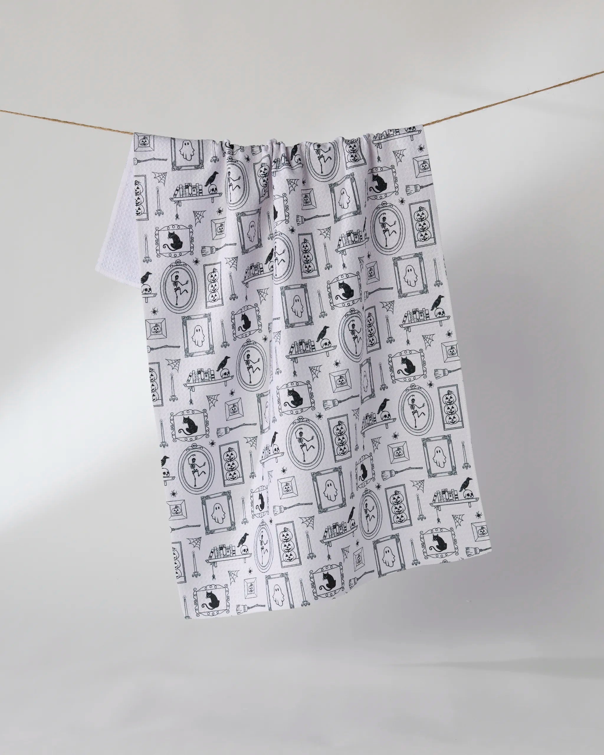 The Geometry "Haunted Gallery" tea towel, featuring black minimalist illustrations on white and made from recycled materials, hangs on a light background.