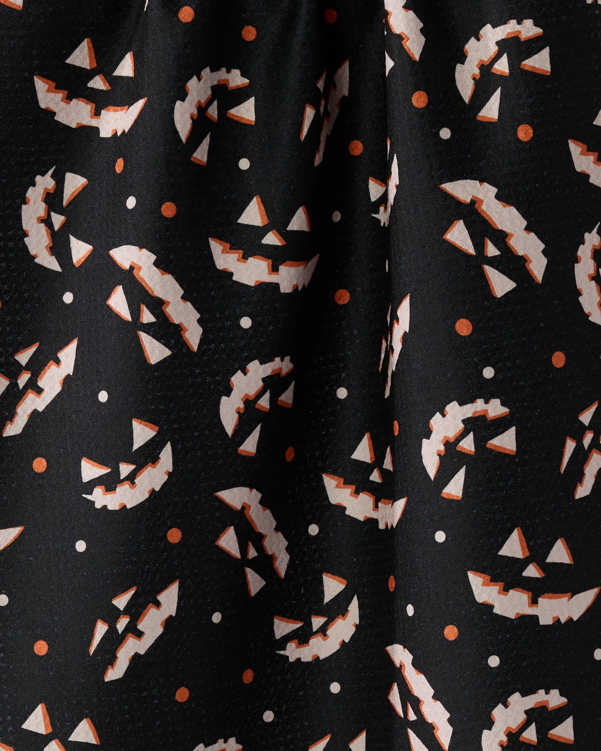 The Geometry Haunted Grin tea towel features black fabric with orange and white jack-o-lantern faces in various orientations and matching dots for a festive Halloween look. Made from recycled materials.