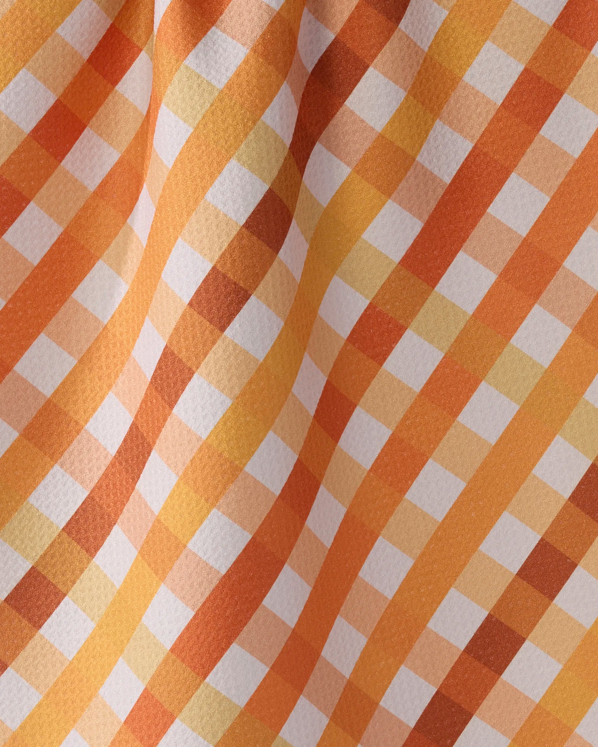 A close-up of Geometry’s Haybales recycled kitchen towel, displaying an orange, yellow, and white checkered pattern with gentle waves and folds creating soft shadows.