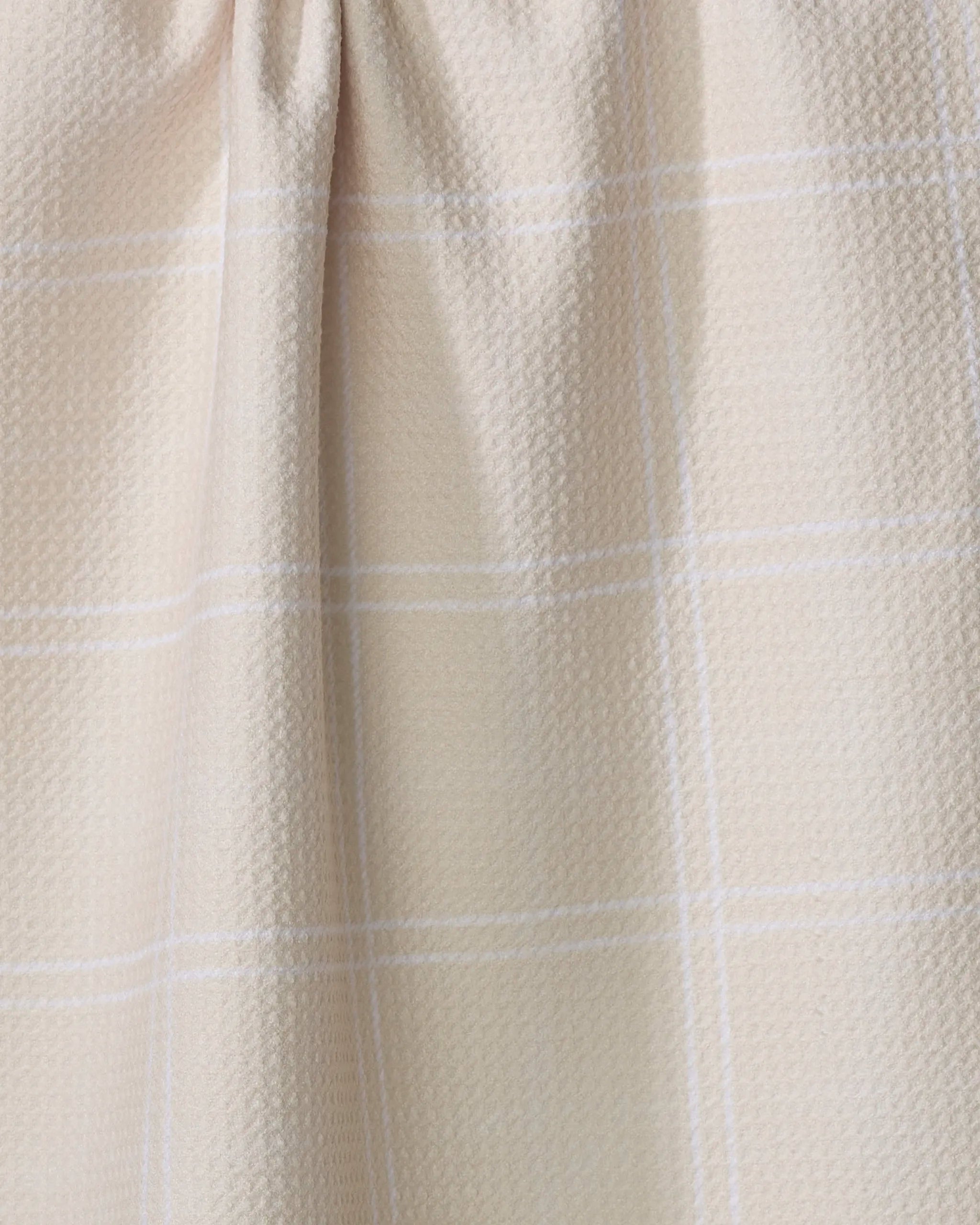 Close-up of the Geometry Hearth Oat tea towel, featuring a beige textured fabric with a subtle white plaid pattern and a gathered seam at the top.