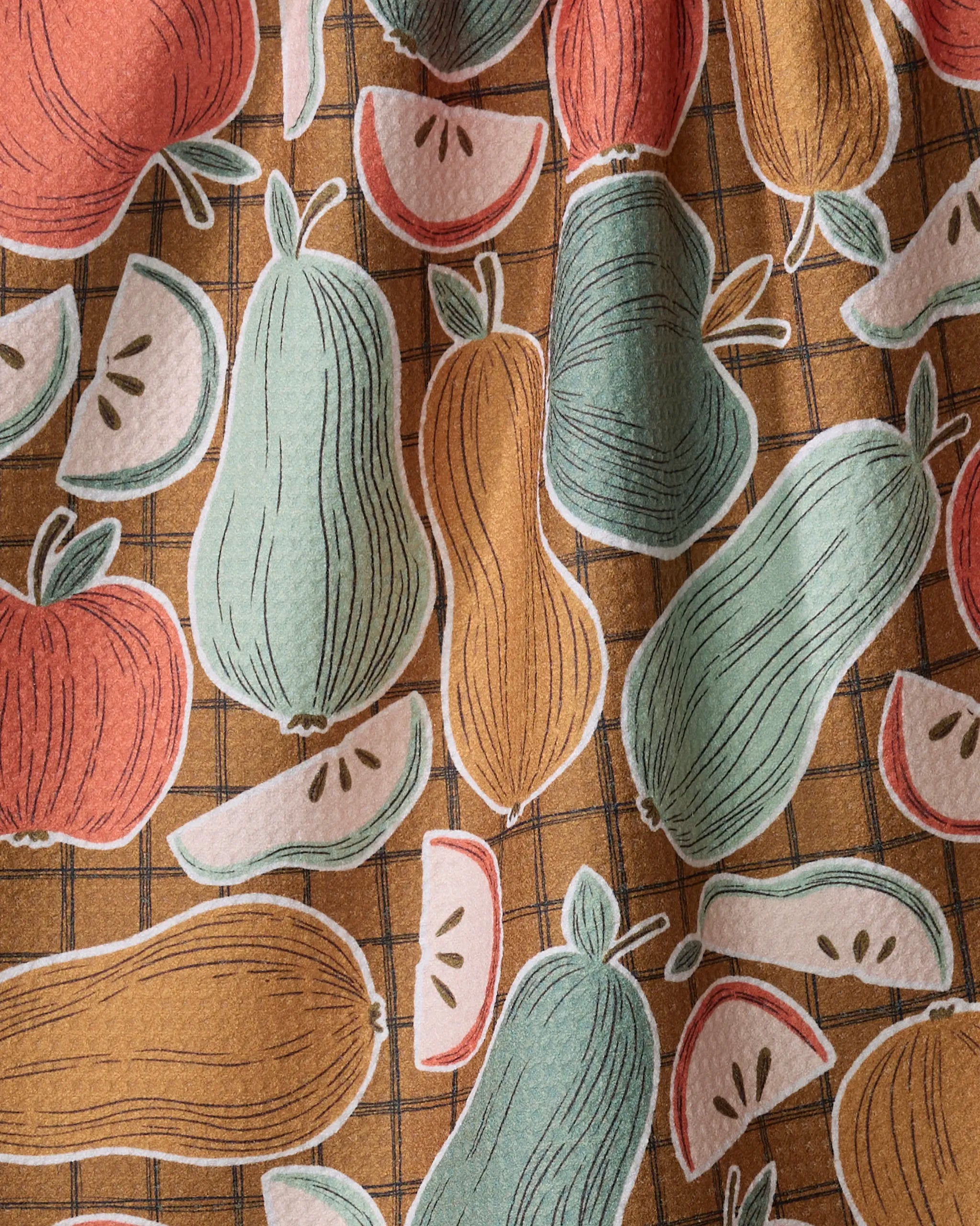 The Heath tea towel by Amy MacCready features apples, apple slices, and gourds in red, green, and yellow on a brown checkered background—perfect as a charming patterned kitchen towel.