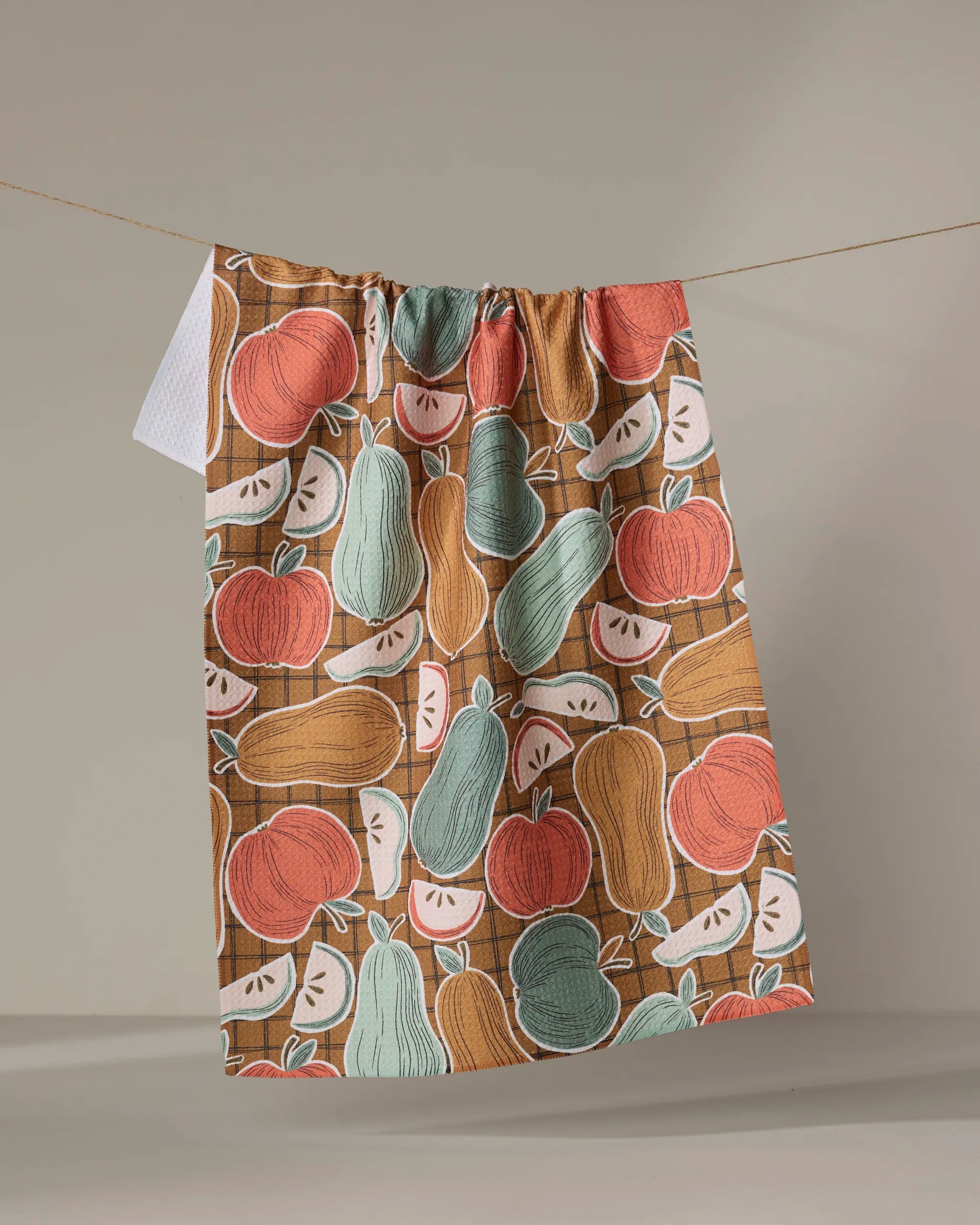 The Heath kitchen towel by Amy MacCready is made from recycled materials and features a vibrant illustrated pattern of pumpkins, squash, pears, and apples in orange, green, and cream tones against a neutral background.