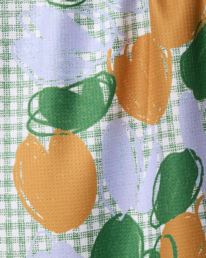 The Hej kitchen towel by Geometry features a recycled, textured design with abstract fruit patterns in green, orange, and light purple on a white and green checkered background.
