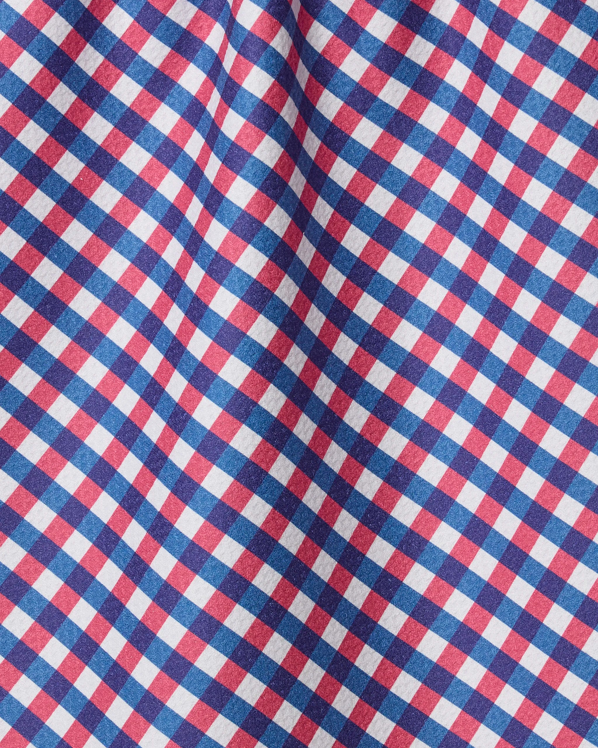 A close-up of the Geometry Heritage Check tea towel reveals a vibrant red, blue, and white plaid pattern in diagonal rows. The slightly wrinkled, ultra-absorbent fabric highlights the towel’s charm and quality.