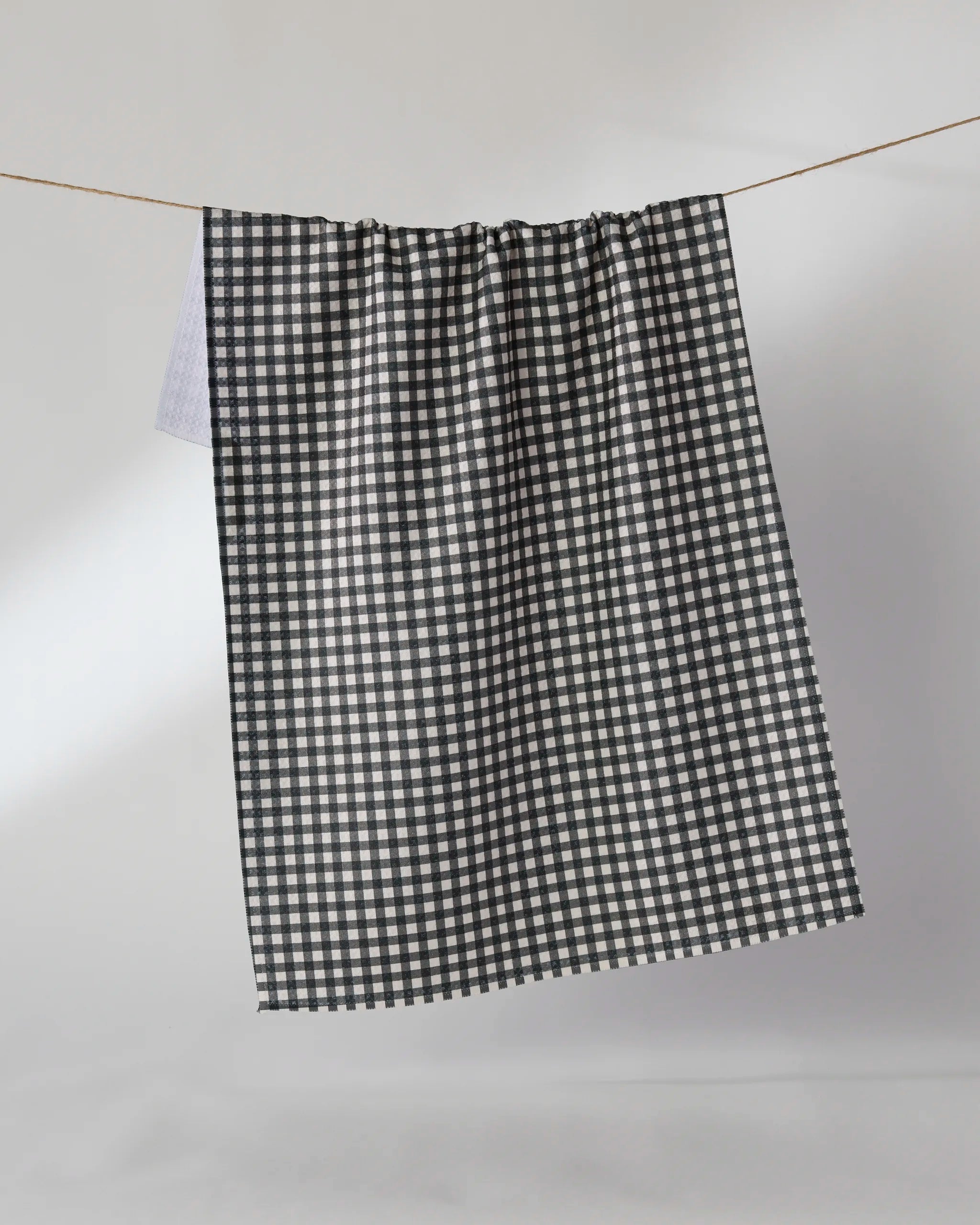 The Geometry Heritage kitchen towel, featuring a black and white checkered design, hangs from a string against a plain white background.