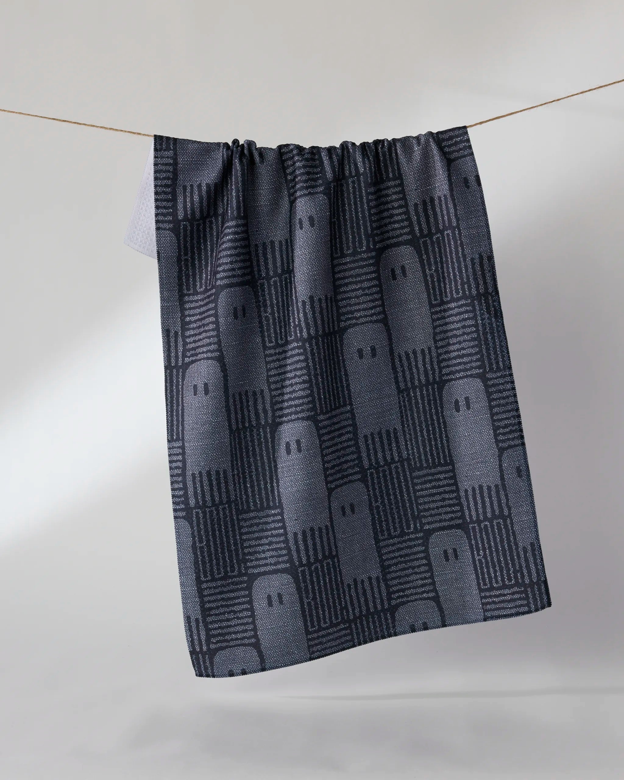 The Geometry Hide and Shriek kitchen towel, made from recycled material, hangs in dark gray with light gray ghost shapes and repeating "BOO" accents.