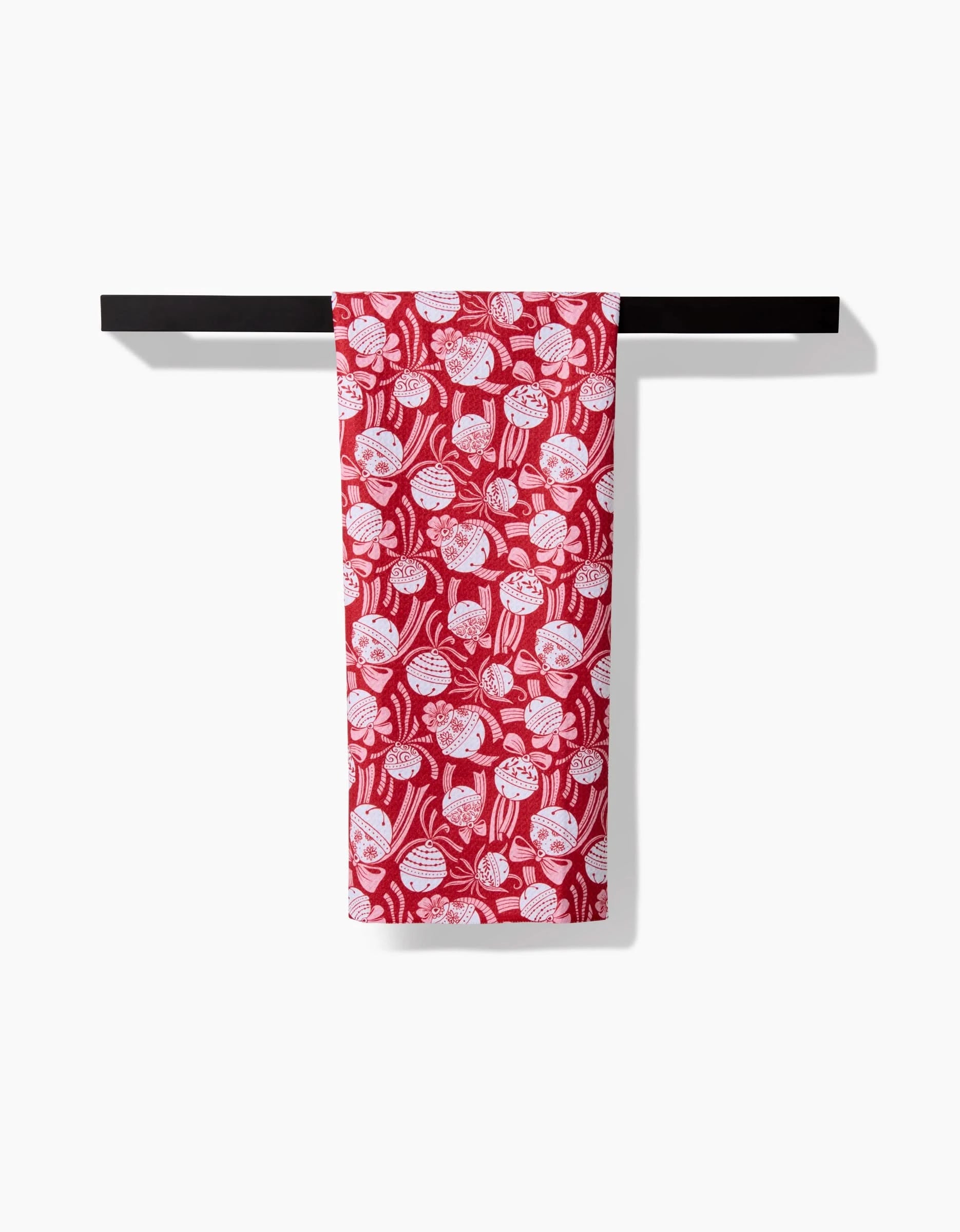 The Holiday Bells Bows tea towel by Sarah Daugherty, featuring a red and white floral and leaf pattern made from recycled materials, hangs neatly over a black rod against a plain white background.