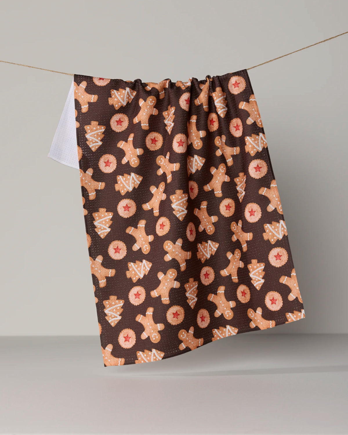 The Geometry “Holiday Cookies” tea towel features a charming gingerbread man, tree, and cookie pattern in brown tones, adding festive cheer to your kitchen. Designed for practicality as well as style, this quick-drying towel hangs beautifully against any neutral background.