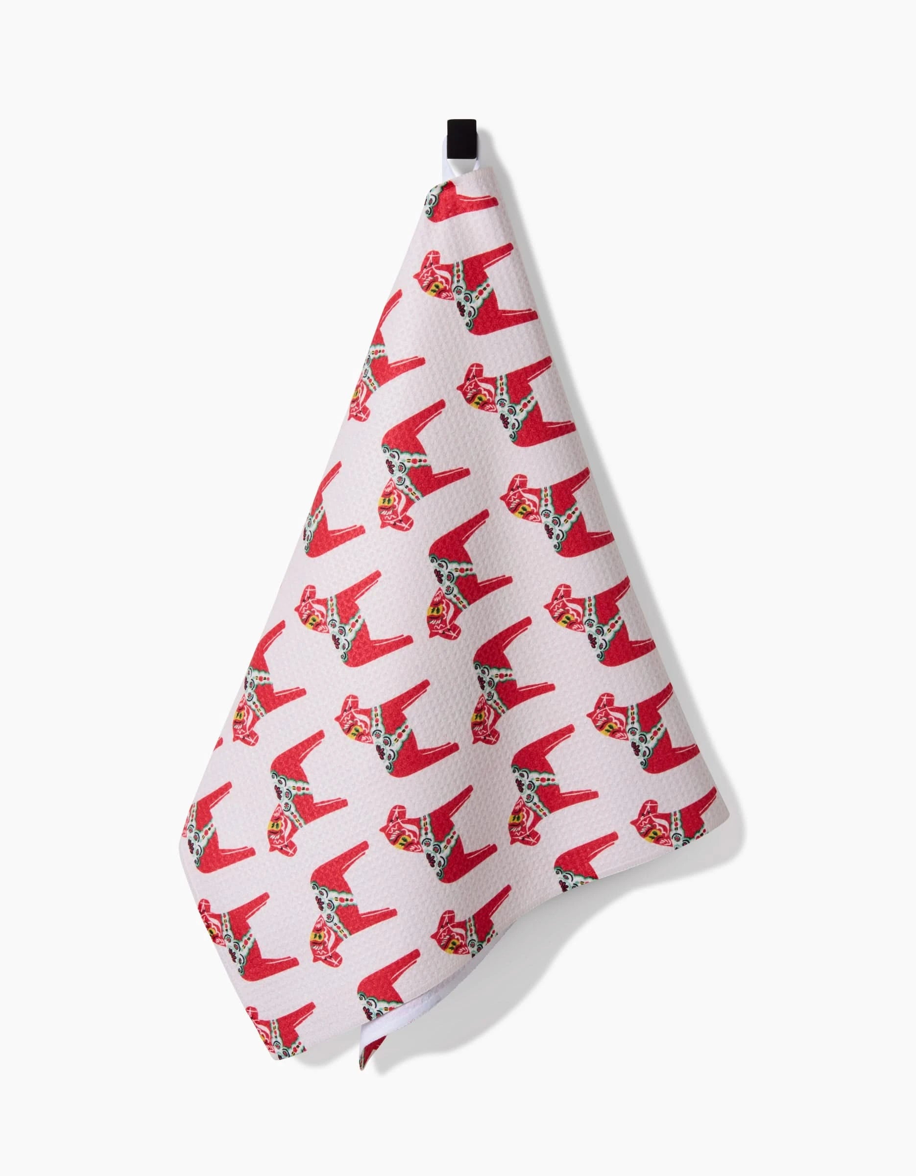 A pink tea towel by Kayla Ann, called the Holiday Dala Horse, hangs from a black loop and features a repeating pattern inspired by festive motifs—crafted from recycled materials for an eco-friendly touch.
