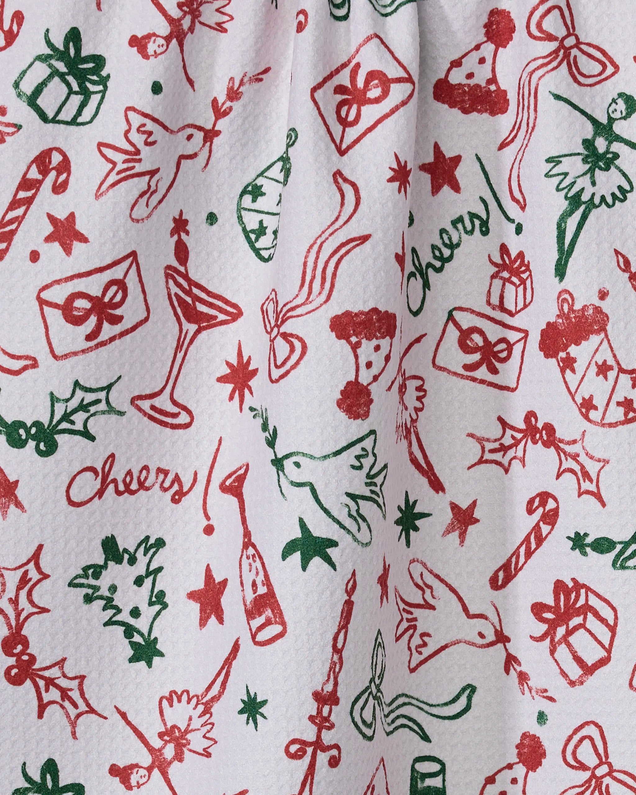 The Geometry Holiday Doodles Multi tea towel is made from recycled materials and features a festive red and green pattern with doves, candy canes, presents, holly, bows, dancing figures, champagne glasses, pie, hats, stars, and "cheers" in cursive.
