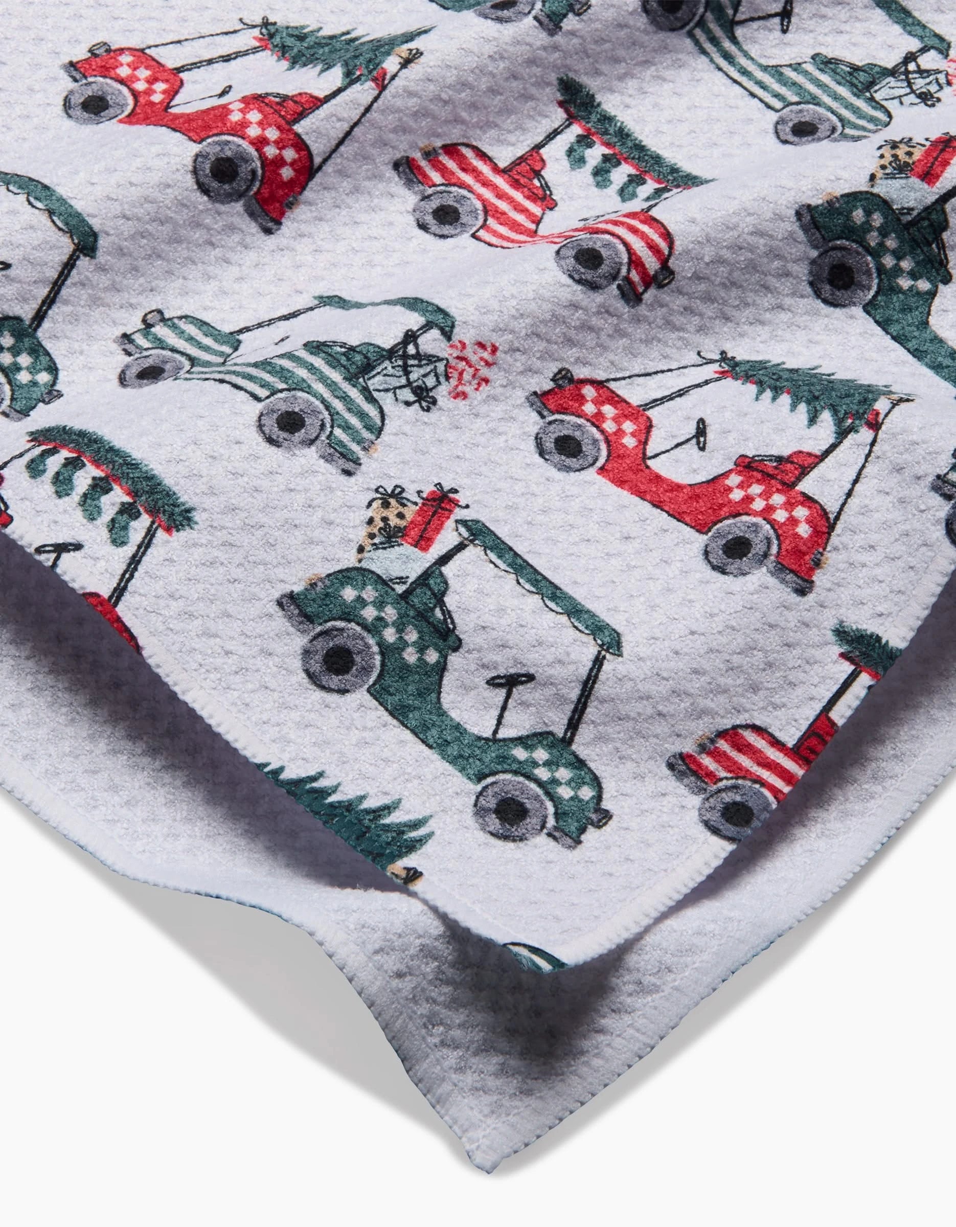 The Charlie Rowan Designs Holiday Golf kitchen towel features a festive white waffle texture with red and green golf carts carrying Christmas trees—an eco-friendly way to add cheerful holiday style to your décor.
