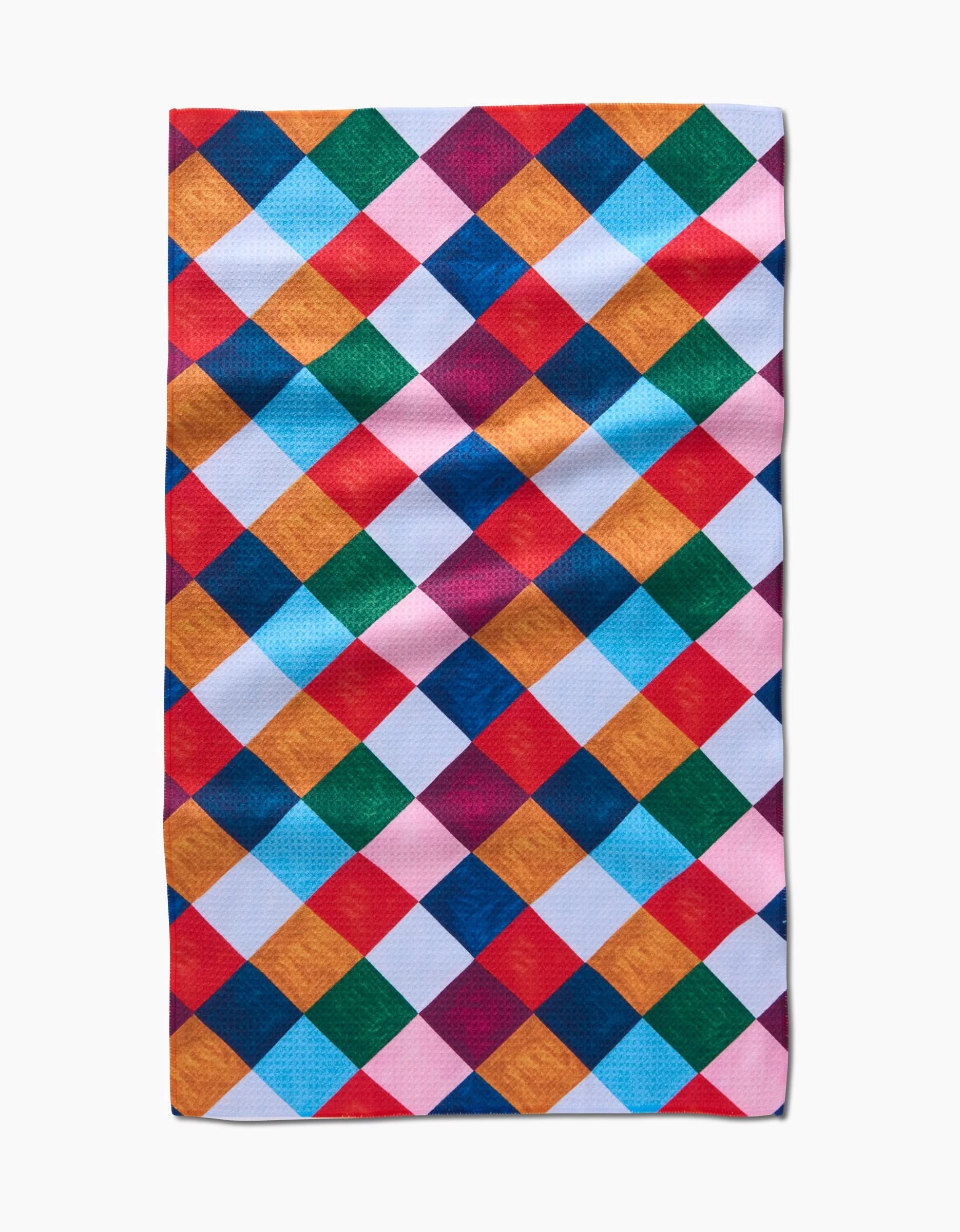 The Holiday Harlequin tea towel by Daria Solak features a vibrant diamond pattern in red, blue, yellow, green, orange, and pink on white. This absorbent rectangular kitchen towel has a slightly wrinkled appearance.