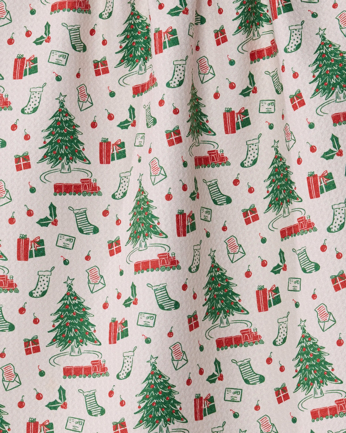 Holiday Jubilee by Geometry is a festive, eco-friendly fabric featuring a repeating pattern of Christmas trees, red toy trains, wrapped gifts, stockings, and letters—all illustrated in cheerful red, green, and white hues. Crafted from recycled materials for sustainable charm, it’s set against a light background with a subtle textured finish.