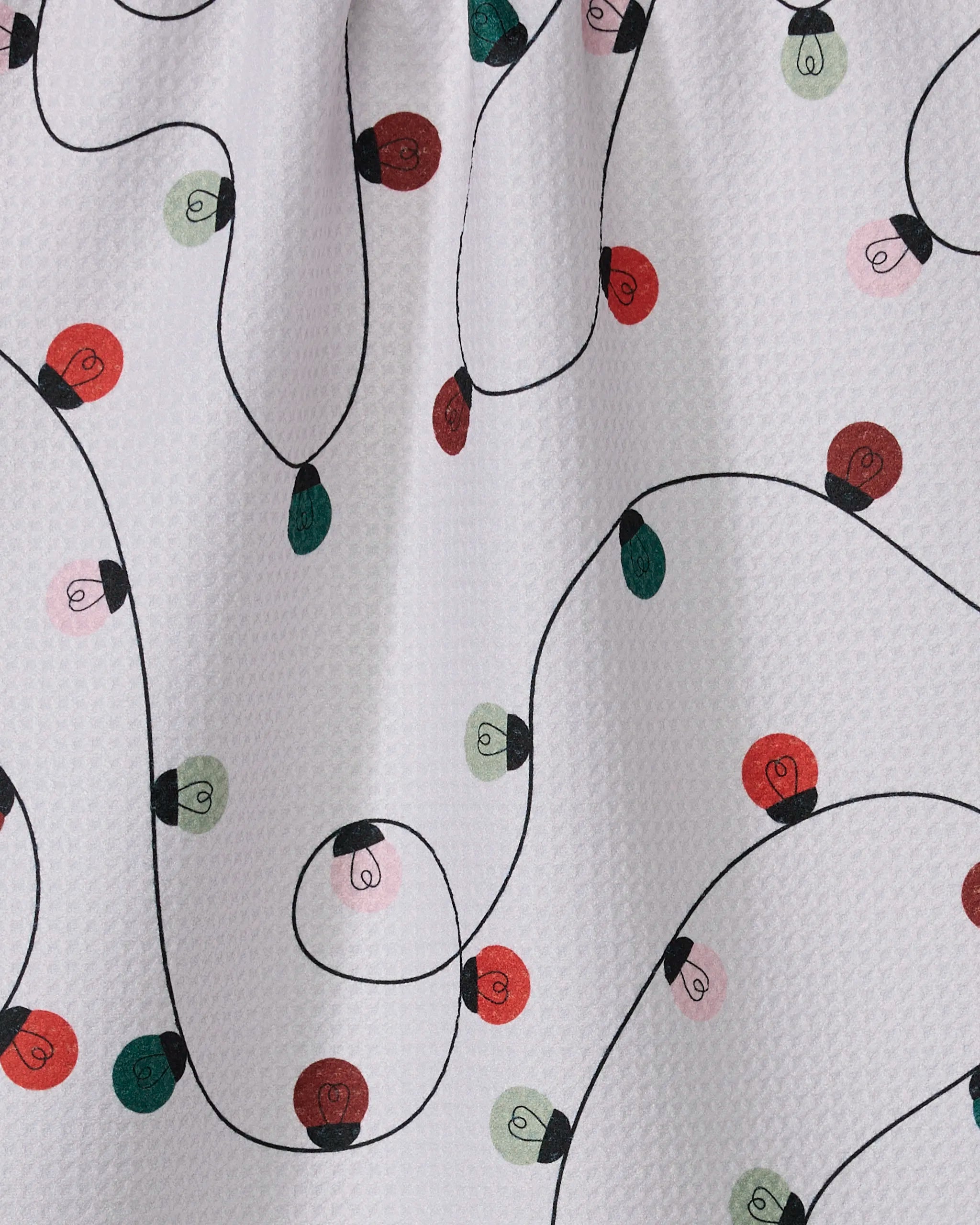 The Geometry Holiday Lights tea towel is white and textured, featuring a festive pattern of red, green, and pink string lights connected by a looping black wire.