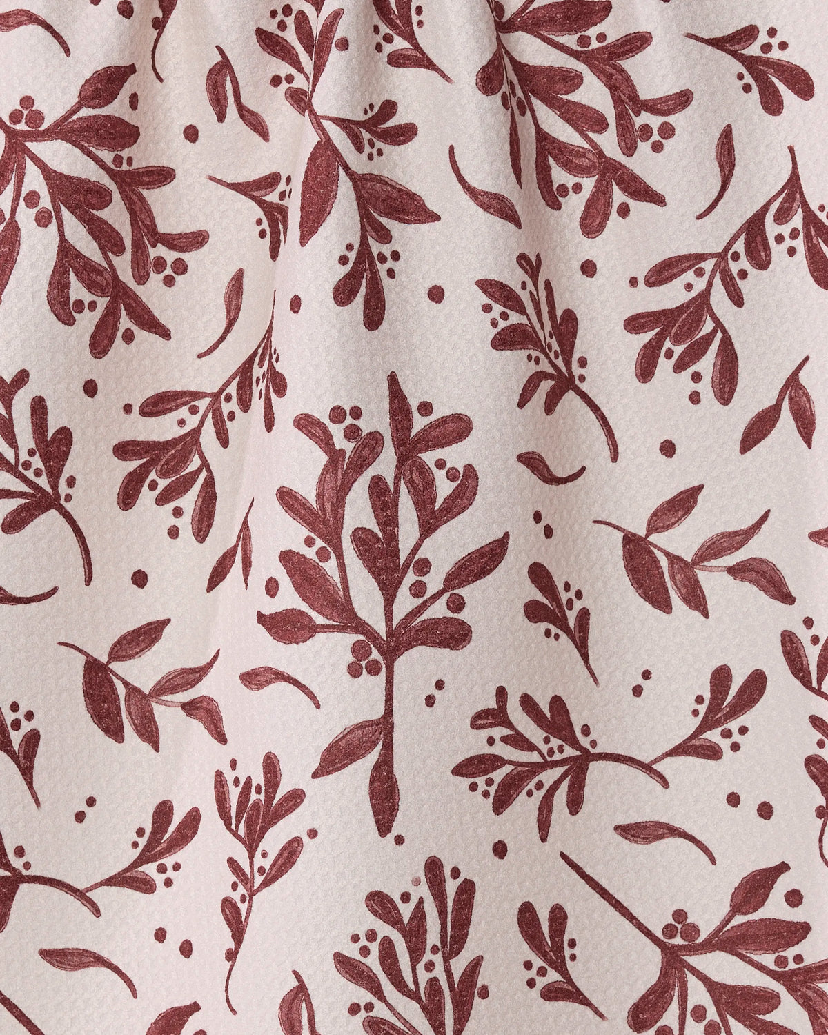 Holly Folly by Geometry features a maroon botanical pattern of leaves and berries on a textured, off-white fabric. This elegant and natural repeating design is perfect for an ultra-absorbent towel or recycled kitchen towel.