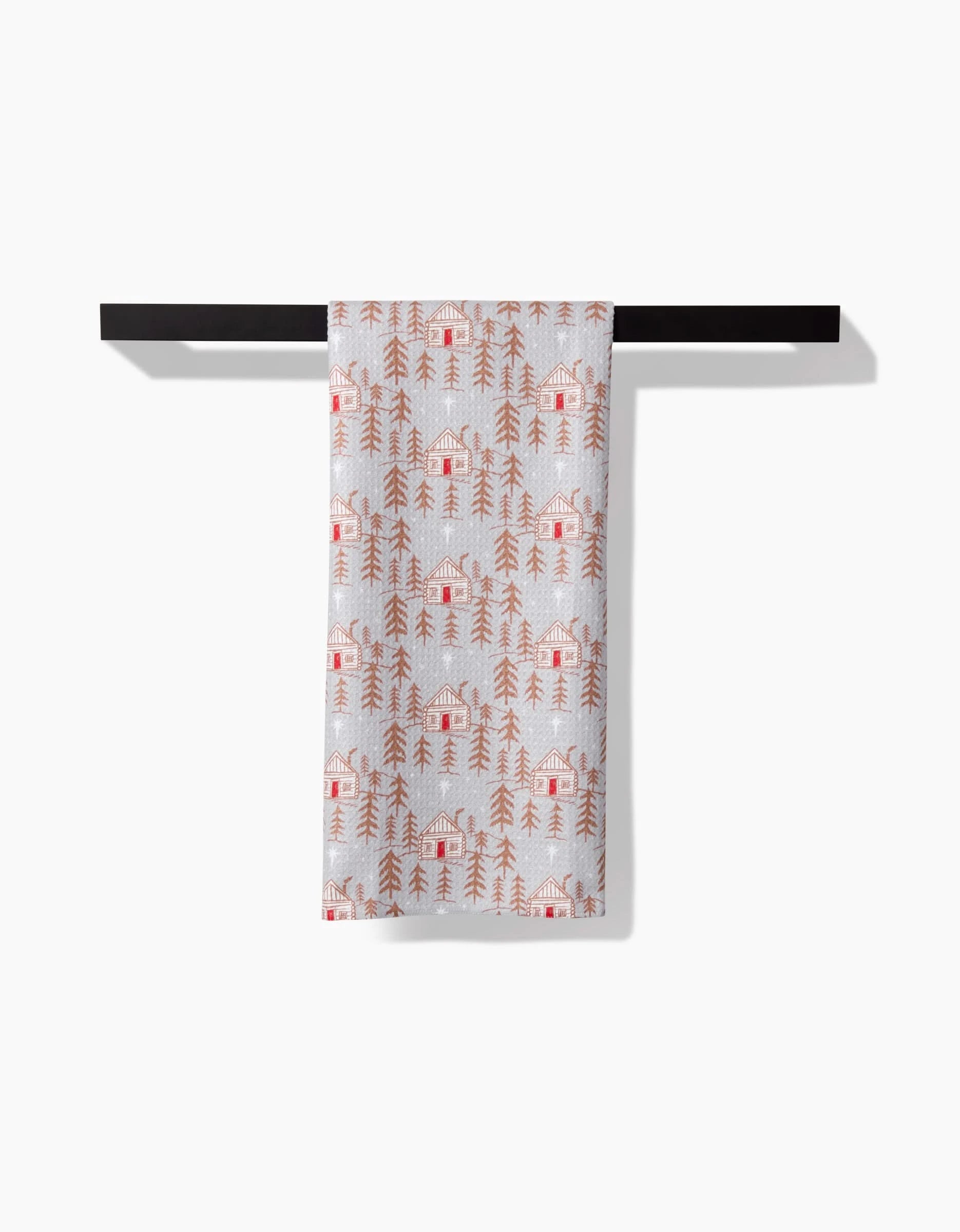 The Roxy Marj Homestead tea towel, featuring an orange cabin and tree design and made from recycled materials, is neatly draped over a black bar against a plain white background.