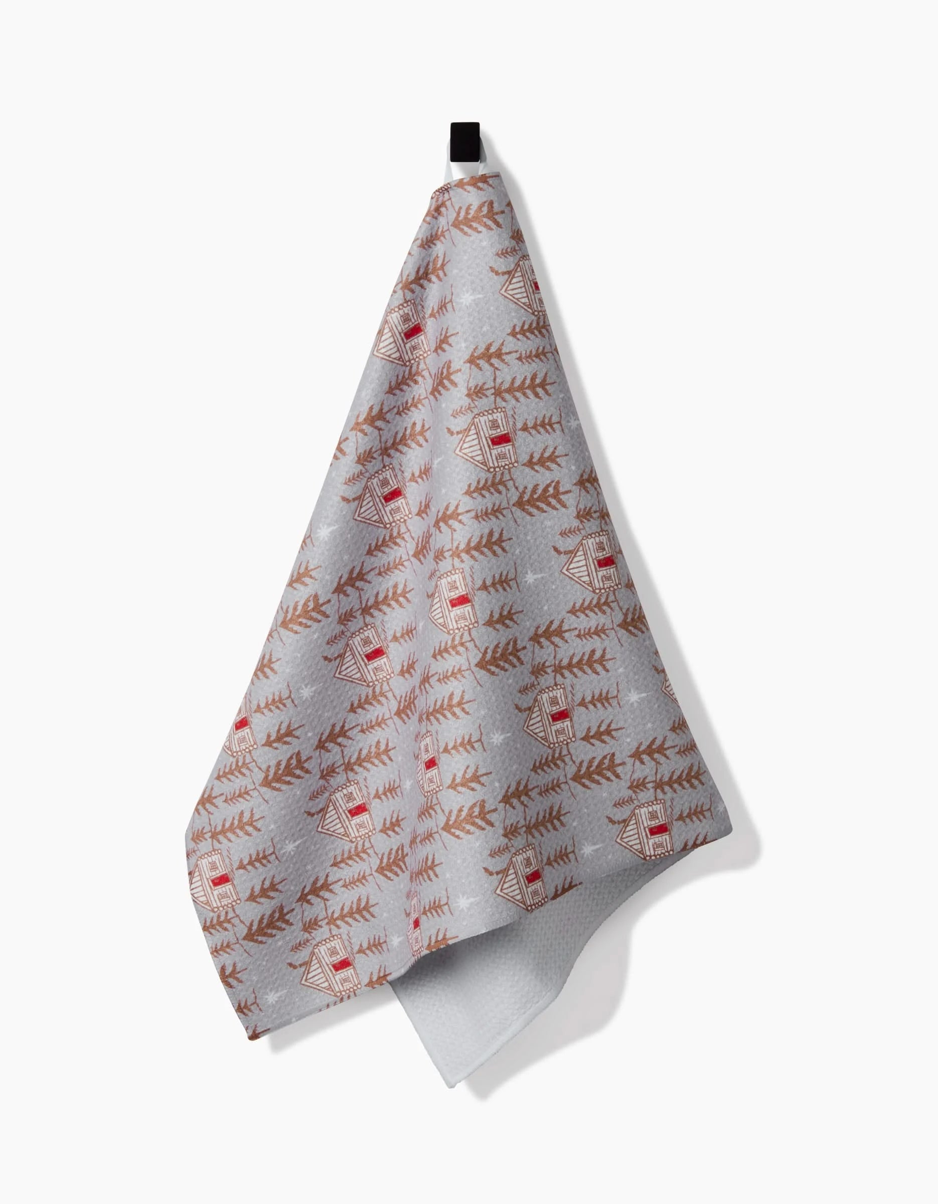 The Homestead tea towel by Roxy Marj, featuring a red and brown cabin and pine tree pattern on gray recycled fabric, hangs from a black loop against a white background.