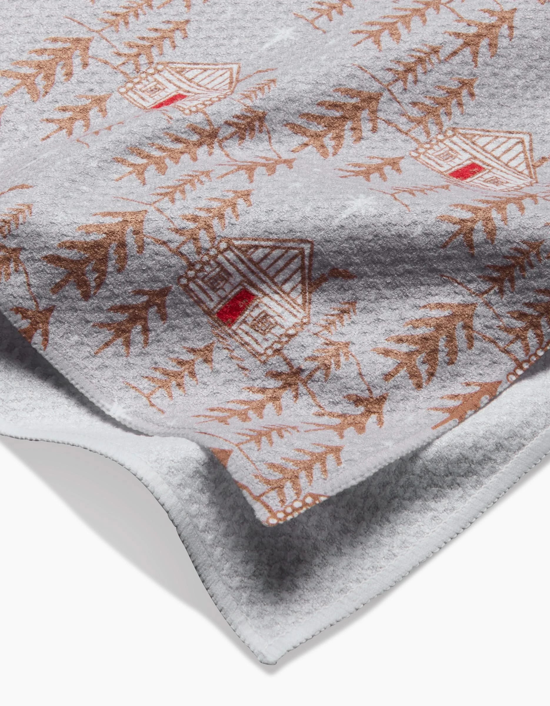 The Homestead blanket by Roxy Marj is a soft gray throw made from recycled materials, decorated with brown leaves and charming small cabins with red doors and windows.