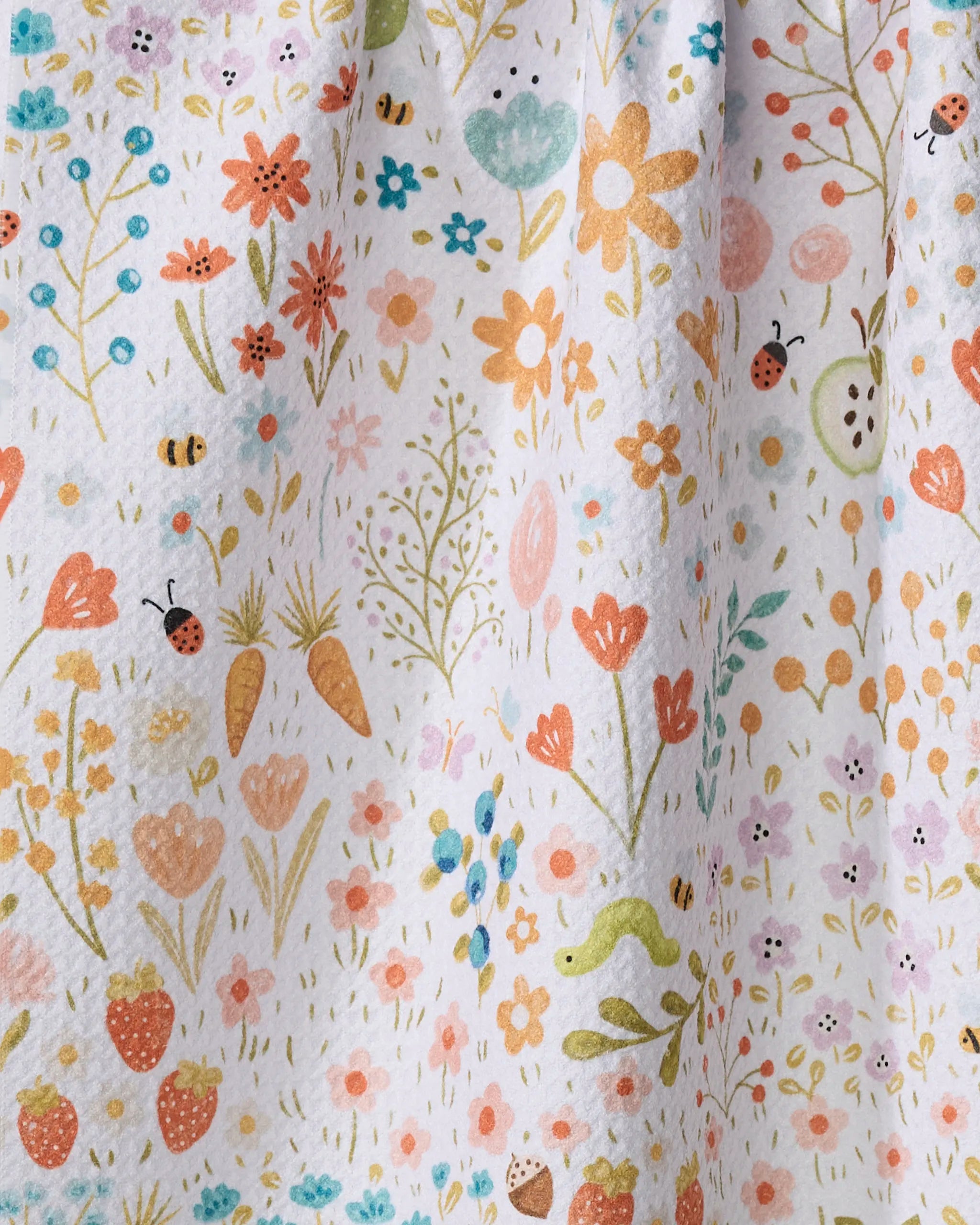 Sara Mari’s “Honeybee Heaven” is a kitchen tea towel crafted from recycled materials, featuring a spring-inspired design with flowers, strawberries, carrots, ladybugs, bees, small plants, and a green snake on a white background.