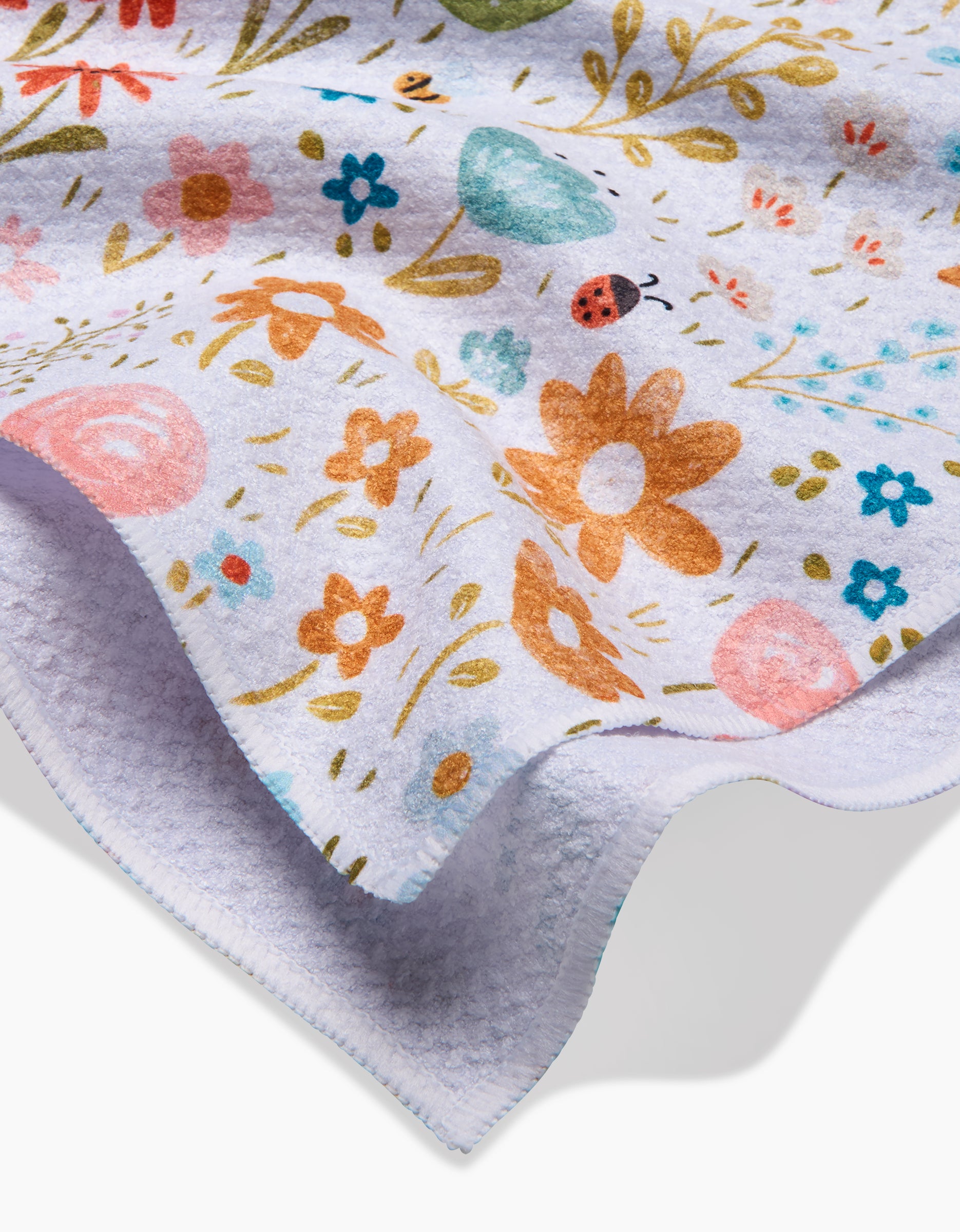 A close-up of the Sara Mari Honeybee Heaven fleece blanket shows its colorful floral and nature print, including flowers, leaves, and a ladybug. Made from eco-friendly materials with neatly stitched edges for lasting quality.