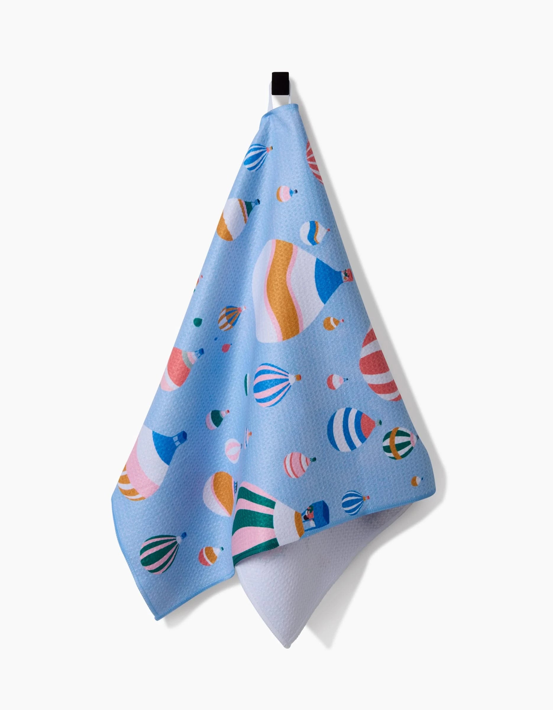 The Ceyda Alasar Hot Air Balloons blue tea towel features a vibrant hot air balloon design and hangs from a black loop against a white background.