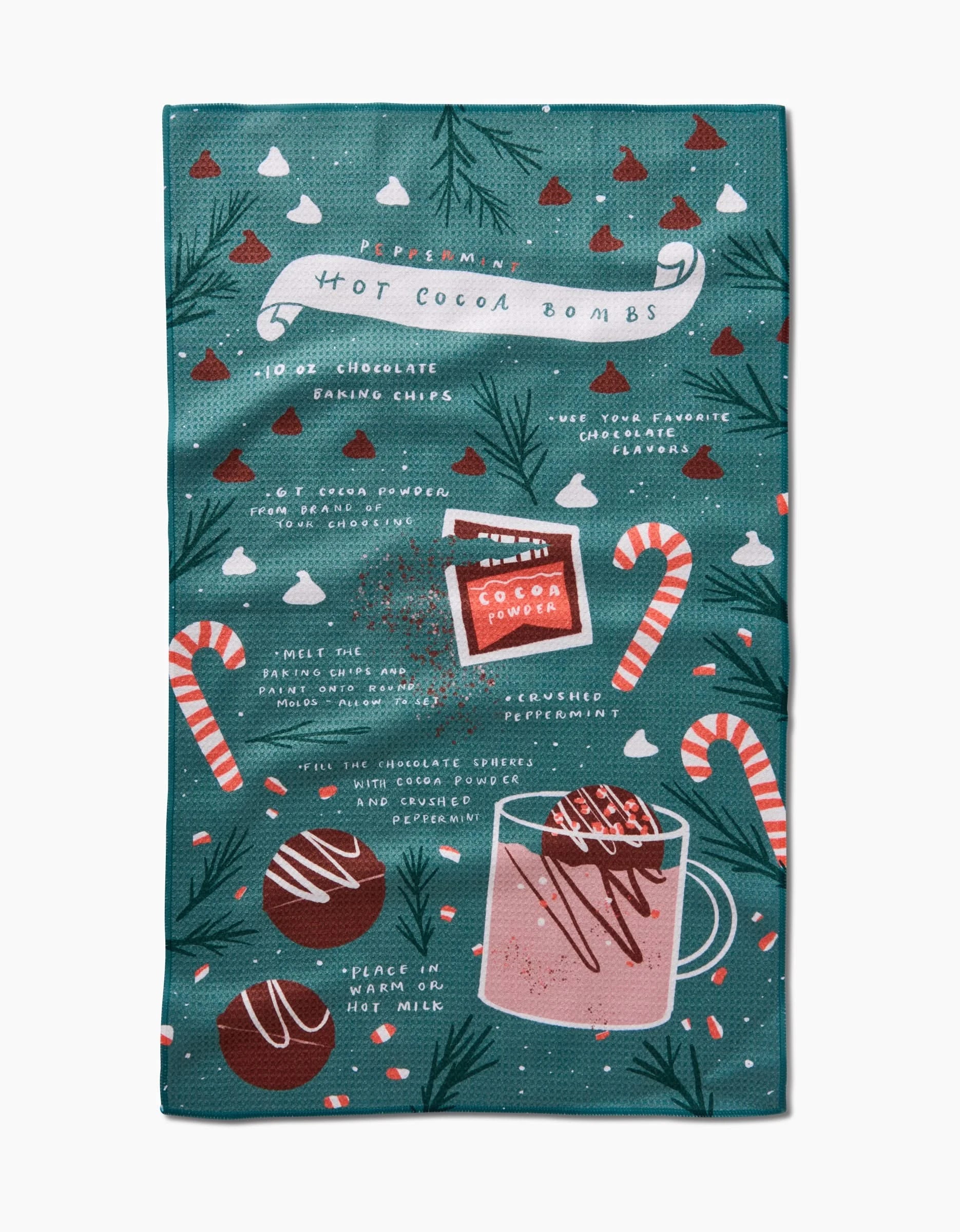 The Hot Cocoa Bomb tea towel by Janna Sue Design features illustrated hot cocoa bomb instructions, chocolate bombs, a mug, candy canes, and pine branches on green—a festive, absorbent addition to your holiday kitchen!.