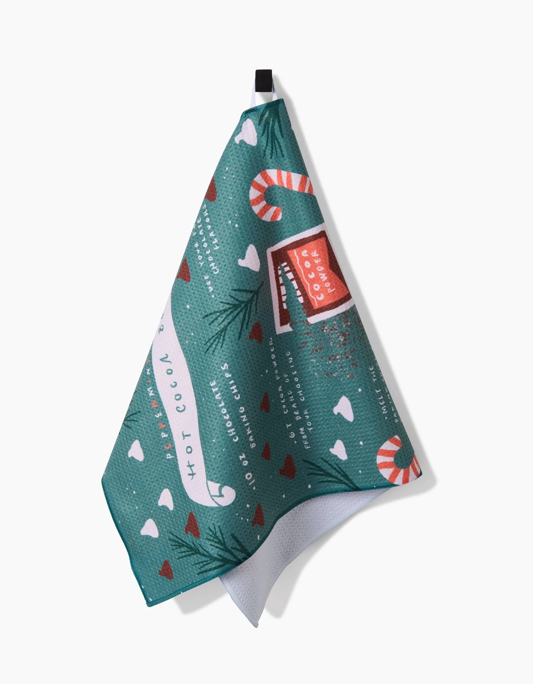 The Janna Sue Design Hot Cocoa Bomb is a festive teal kitchen towel made from recycled materials, featuring candy canes, red hearts, pine branches, and hot cocoa mugs hanging by a black loop against a white background.