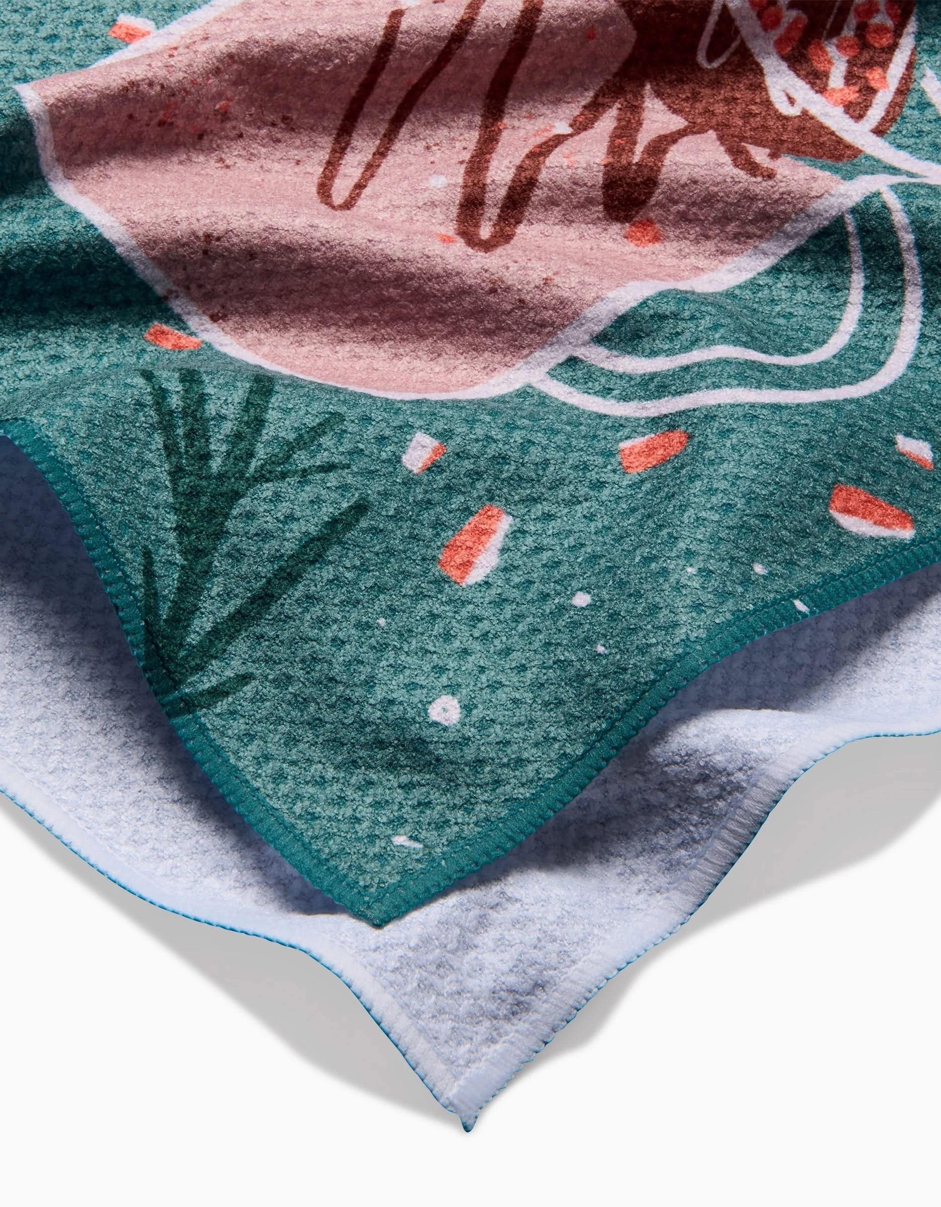 A close-up of the Hot Cocoa Bomb kitchen towel by Janna Sue Design, featuring soft recycled fabric with colorful green, pink, and orange abstract patterns and a partially visible blue-edged underside.