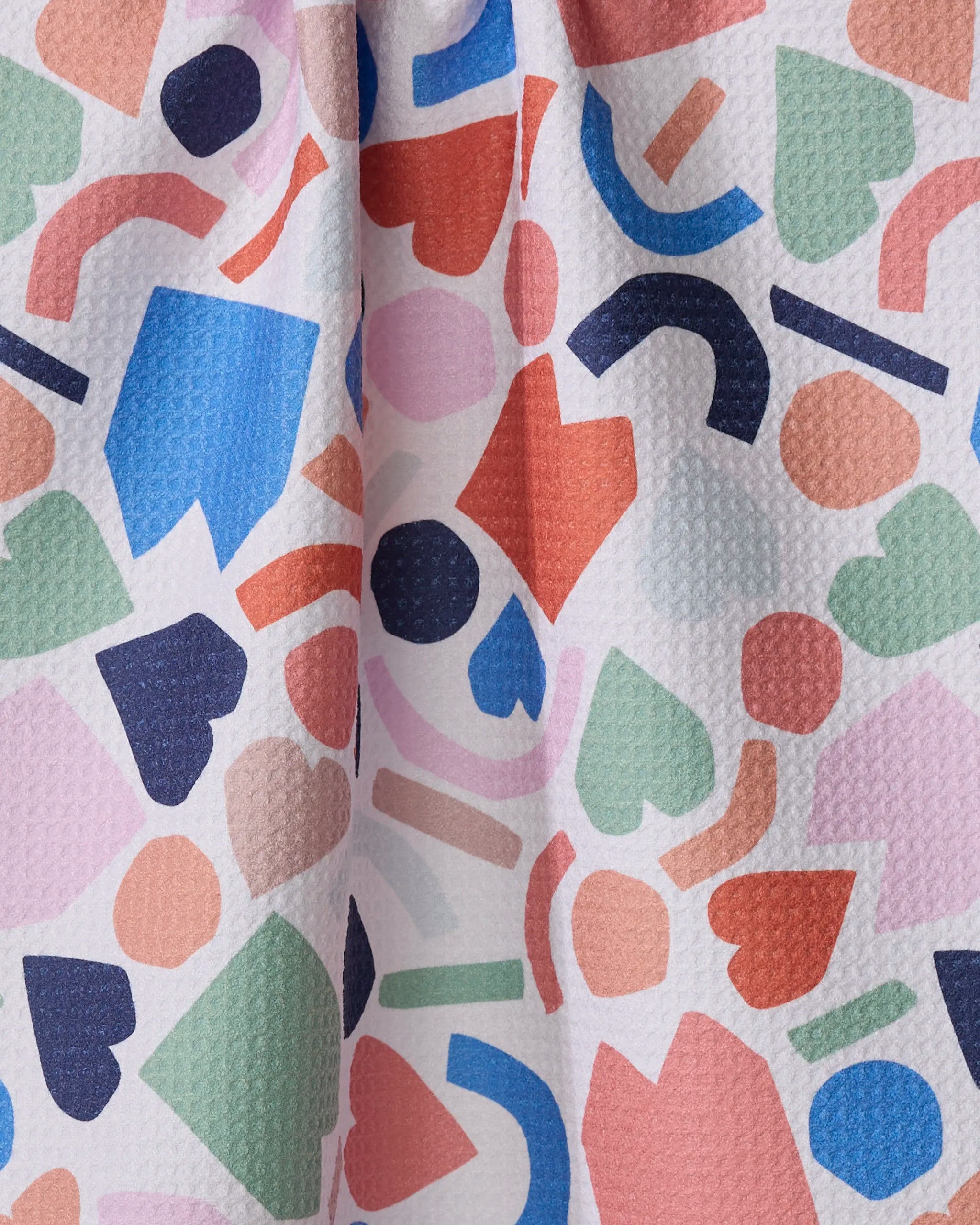 House Party by Claire Iglesias features a colorful abstract pattern with hearts, diamonds, circles, and rectangles in pink, blue, green, red, and navy on a textured white background—a vibrant tea towel for any kitchen.