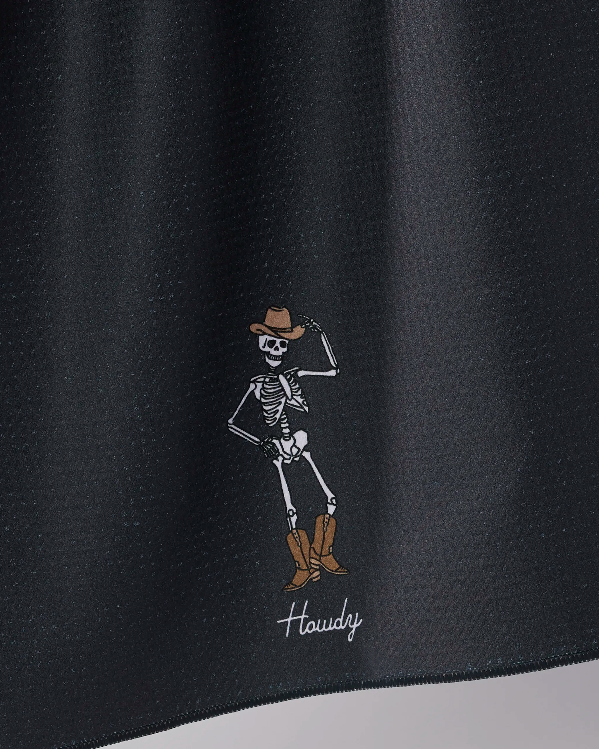 The Howdy Cassondra Black tea towel by Geometry features a cartoon skeleton in a brown cowboy hat and boots tipping its hat above the word "Howdy" in white on black—printed on recycled materials for an eco-friendly touch.