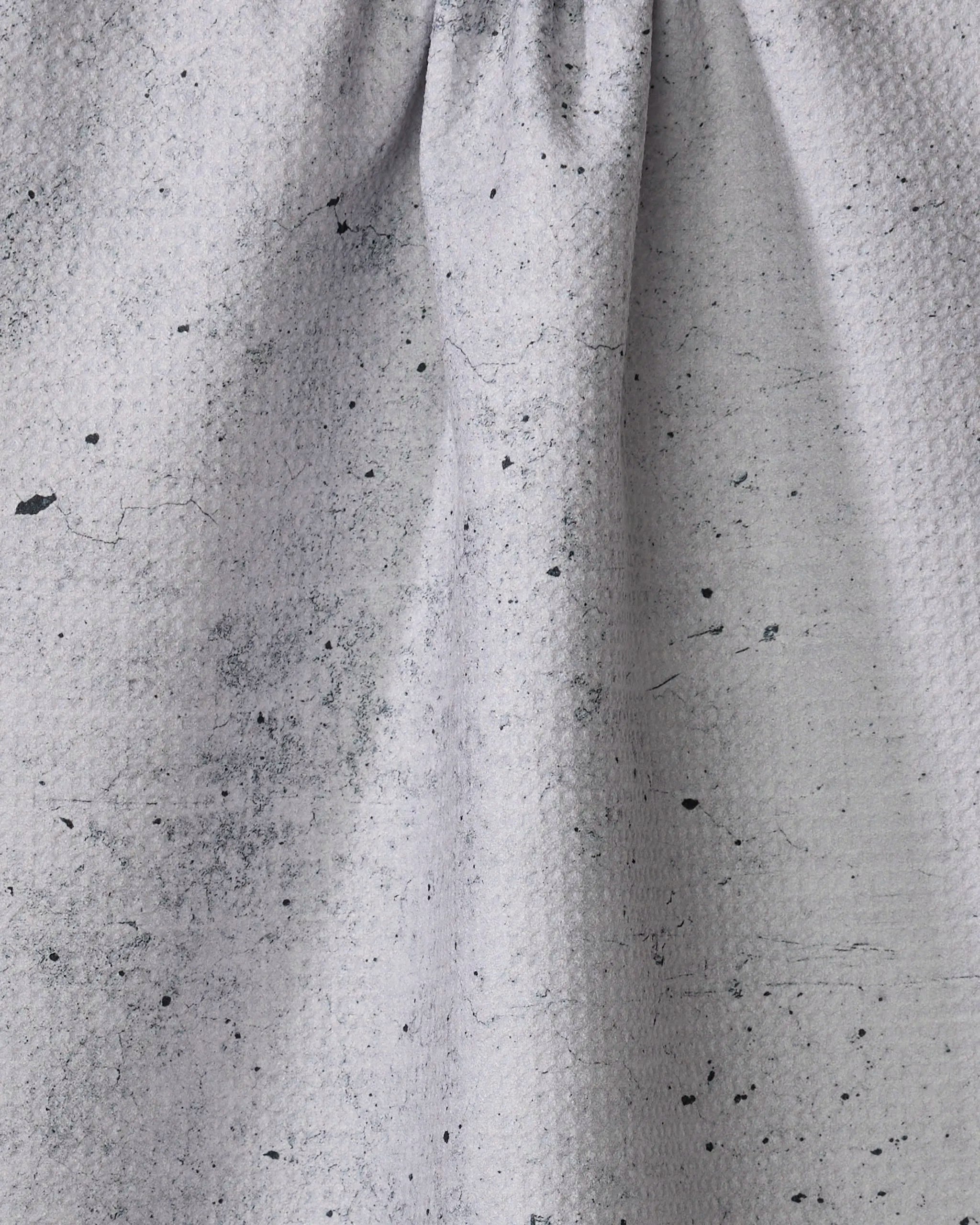 A close-up of the Hudson Grey tea towel by Kailee Wright, in light gray recycled fabric with a gathered seam, subtle textured pattern, and dark paint-like speckles.
