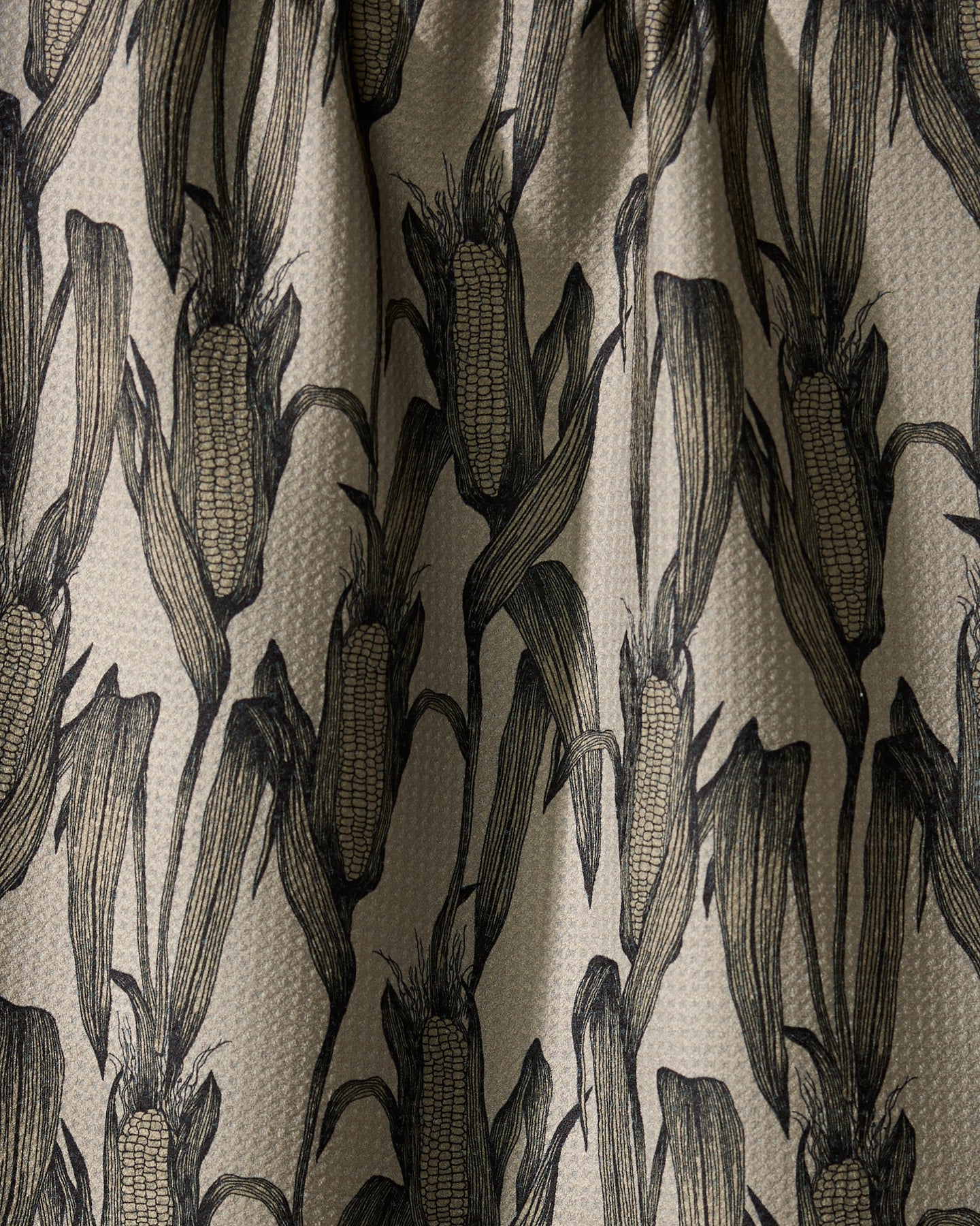 A close-up of Geometrys Husk fabric, featuring black line-drawn corn-on-the-cob motifs on beige—ideal as a stylish kitchen tea towel with its textured, repeating pattern.