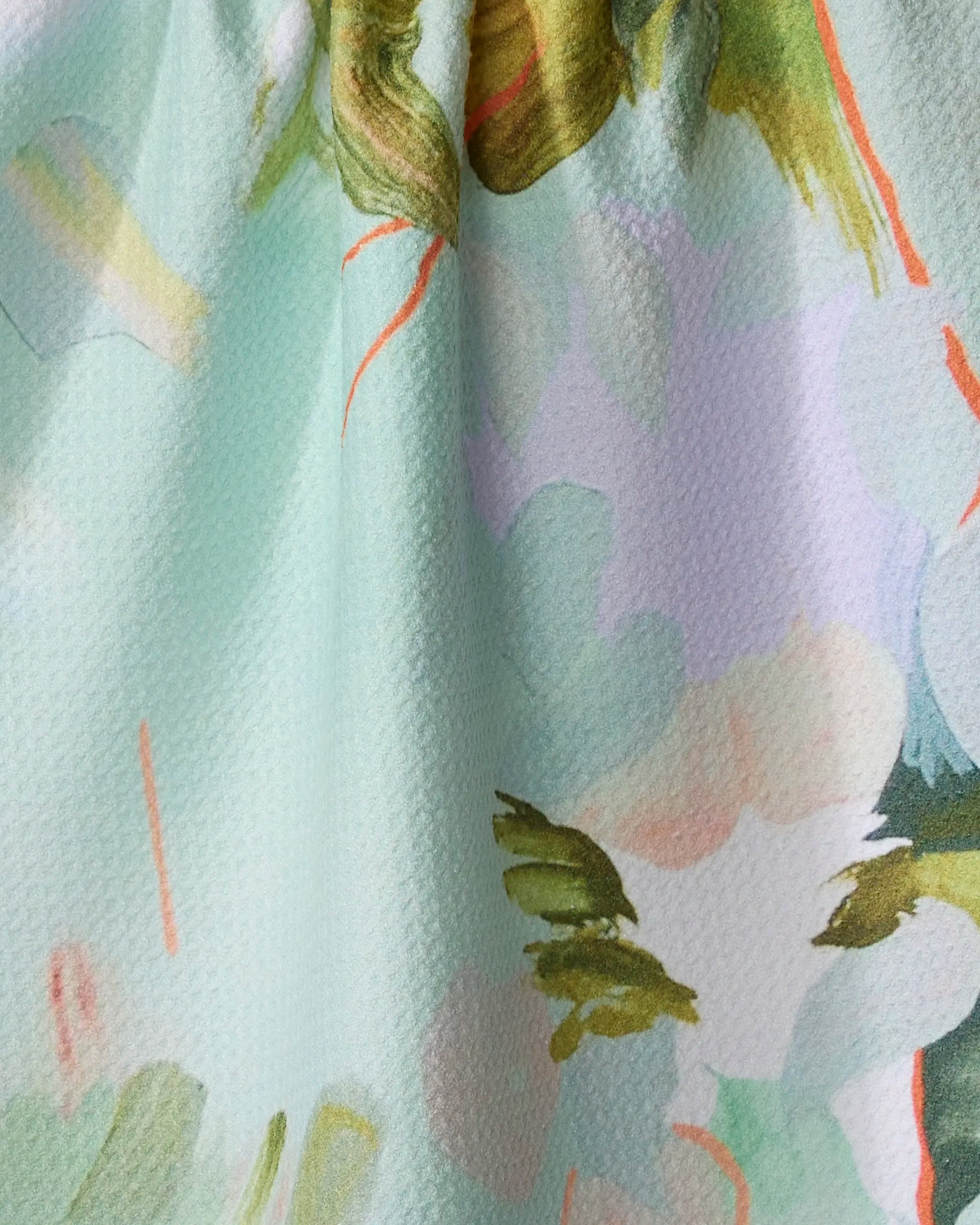 Close-up of Kristina Baker’s "If I Were An Orchard" recycled kitchen towel, featuring an abstract watercolor floral pattern in green, peach, and orange on light aqua. The softly gathered fabric creates gentle folds and textured shadows.