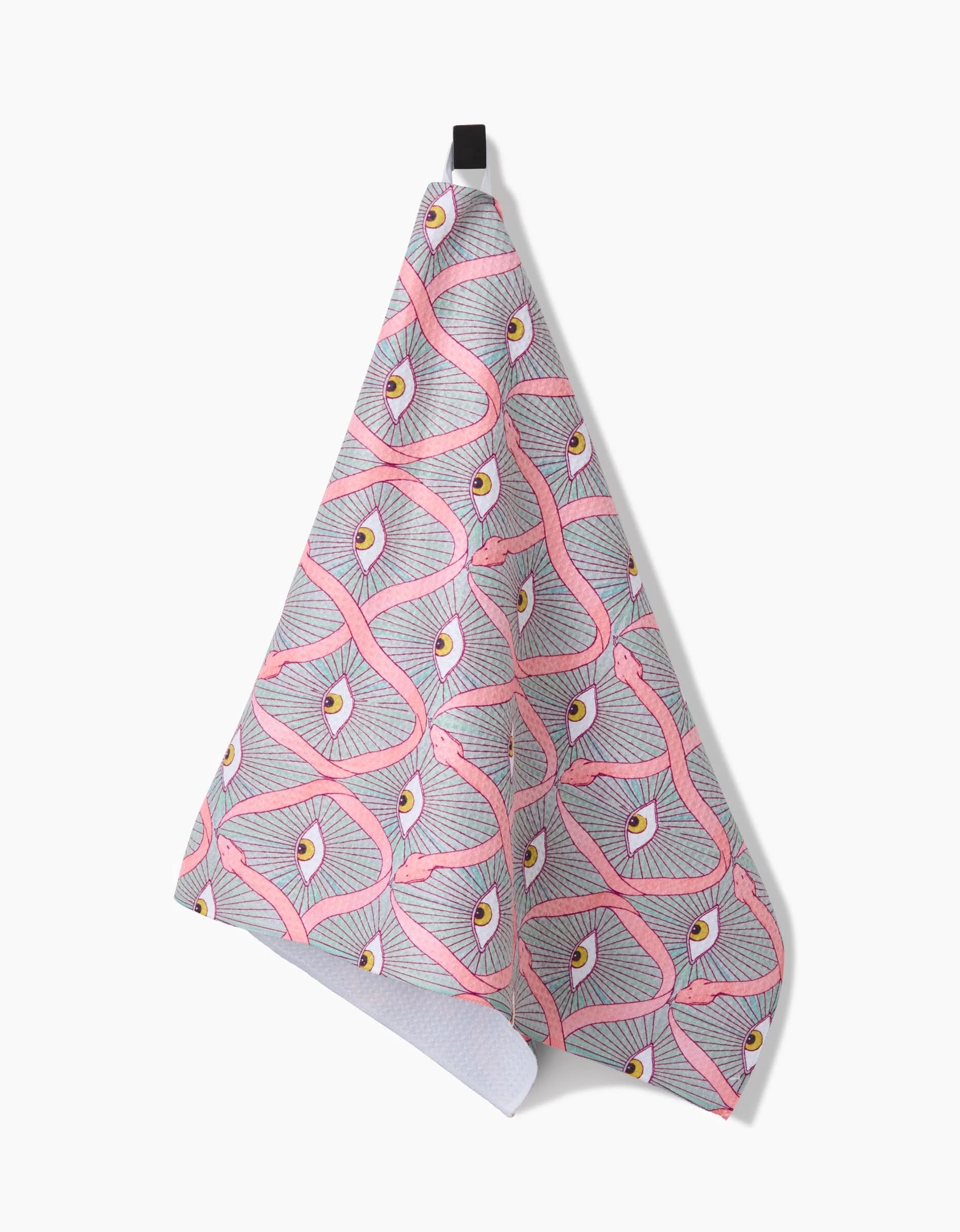 The Illusionist tea towel by Maayan Alper-Swan hangs from a black loop and features a pink snake pattern with yellow and white eyes on light gray Geoweave fabric.