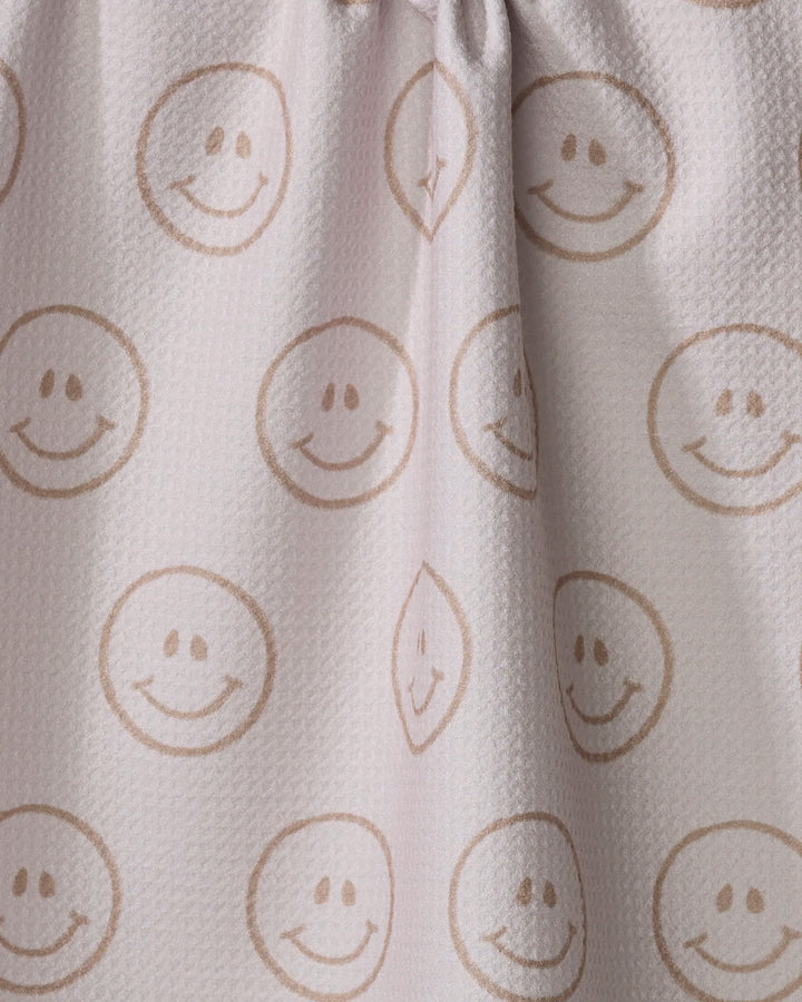 The "I'm Blushing" tea towel by Kelsi Fullmer is made from recycled materials and features a light-colored, textured fabric with brown smiley faces in circles. Soft folds form where the top is slightly gathered for added charm.