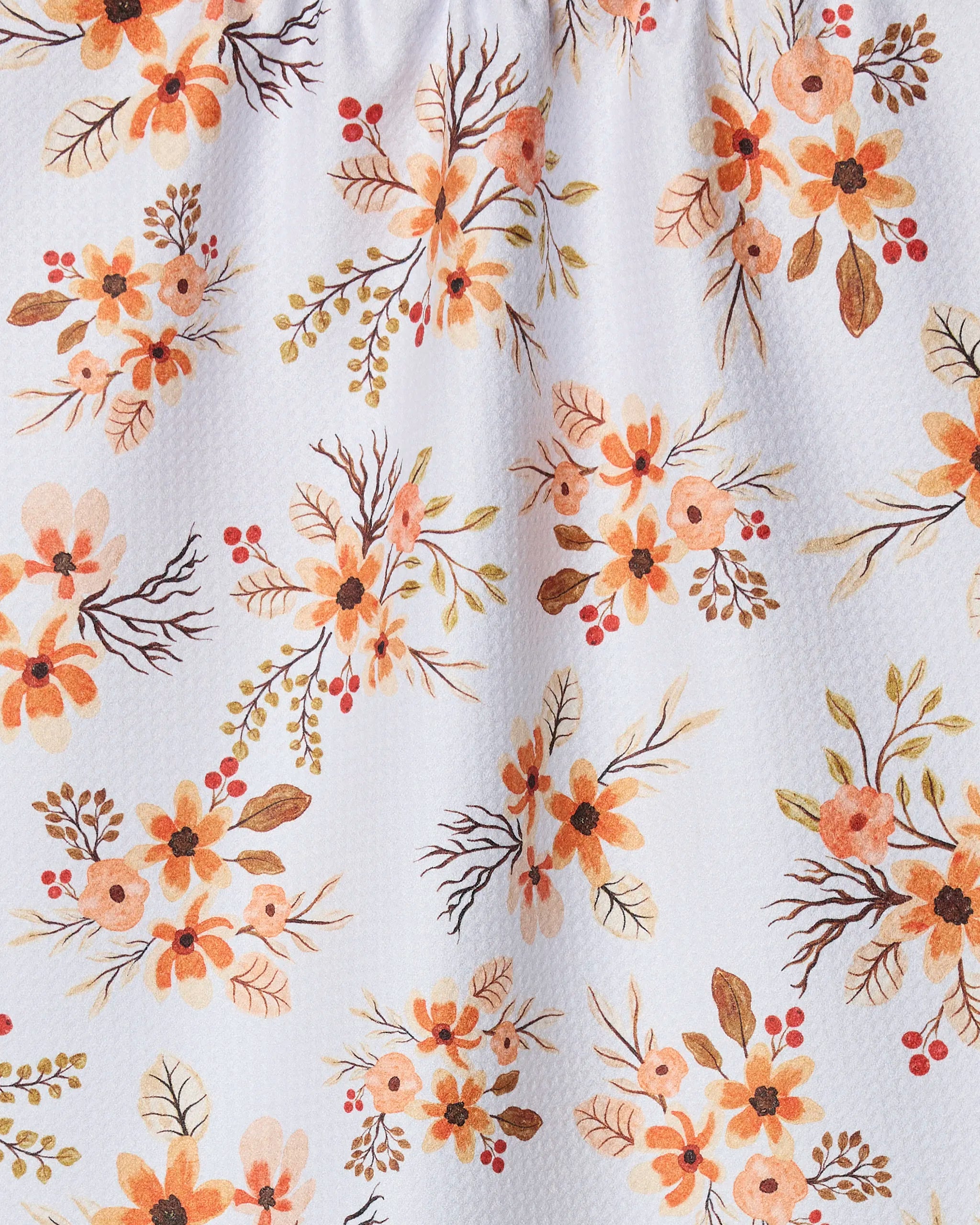 The "In Bloom" tea towel from Vaishali Design Studio is crafted from recycled materials and features a soft, autumn-inspired floral design with orange, peach, and brown watercolor-style flowers, leaves, and branches on a white textured background.