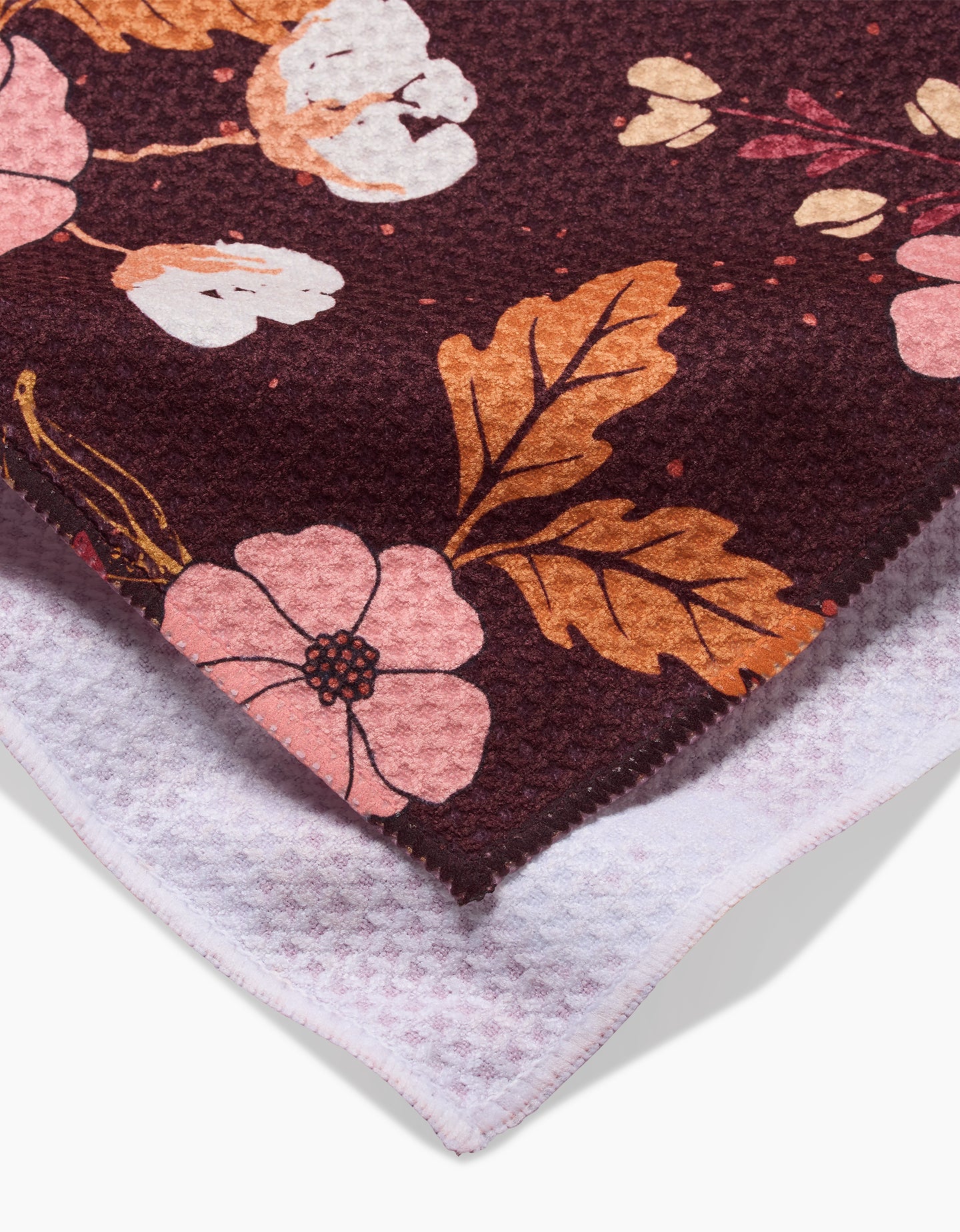 A close-up of Ashley Celenas In The Oaks recycled kitchen towel, featuring a textured maroon surface with pink, white, and orange floral prints and a soft light purple underside.