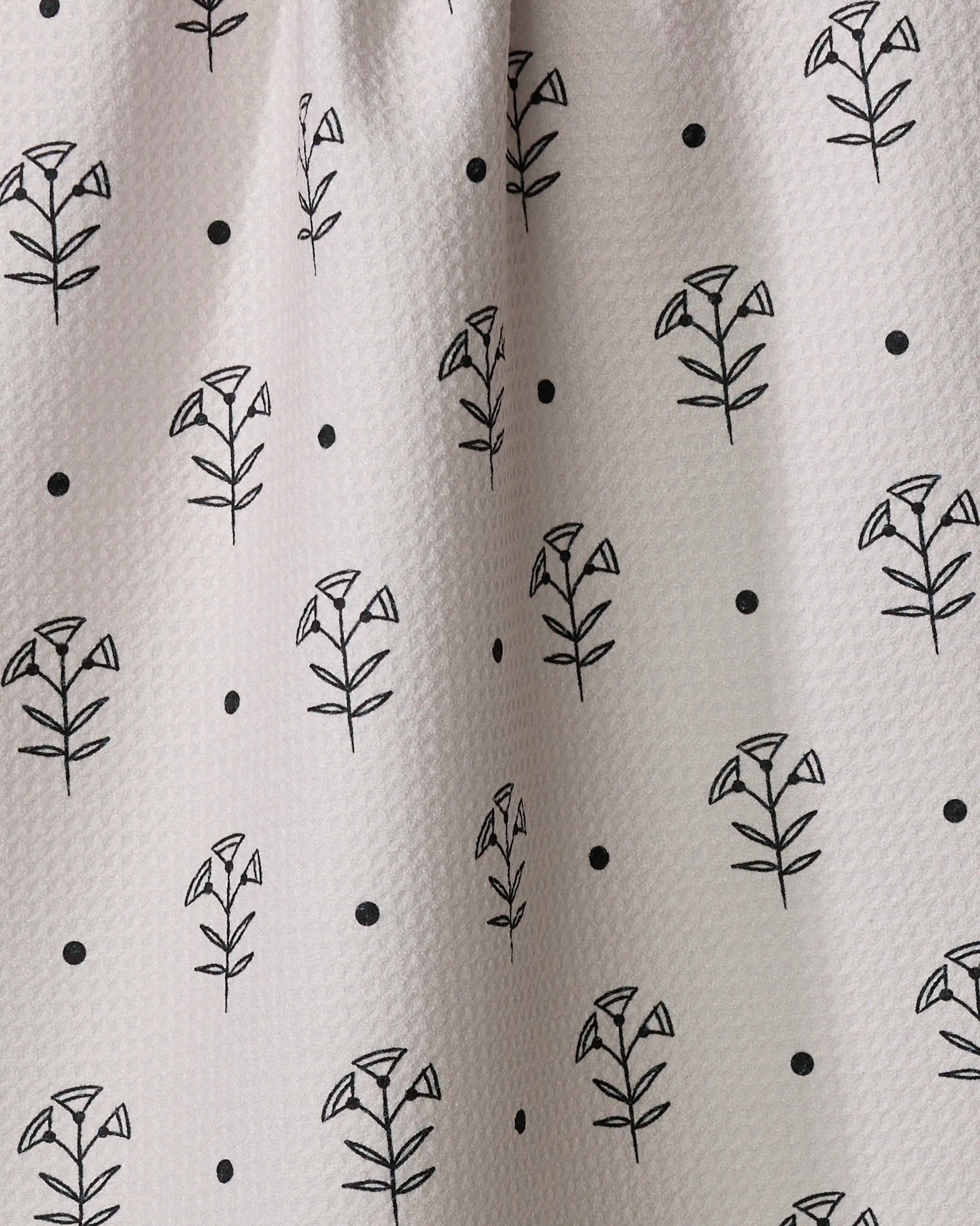 Close-up of Cole Strem's Inked Bloom dish towel, showcasing white textured fabric with a regular grid of simple black floral patterns and small dots.