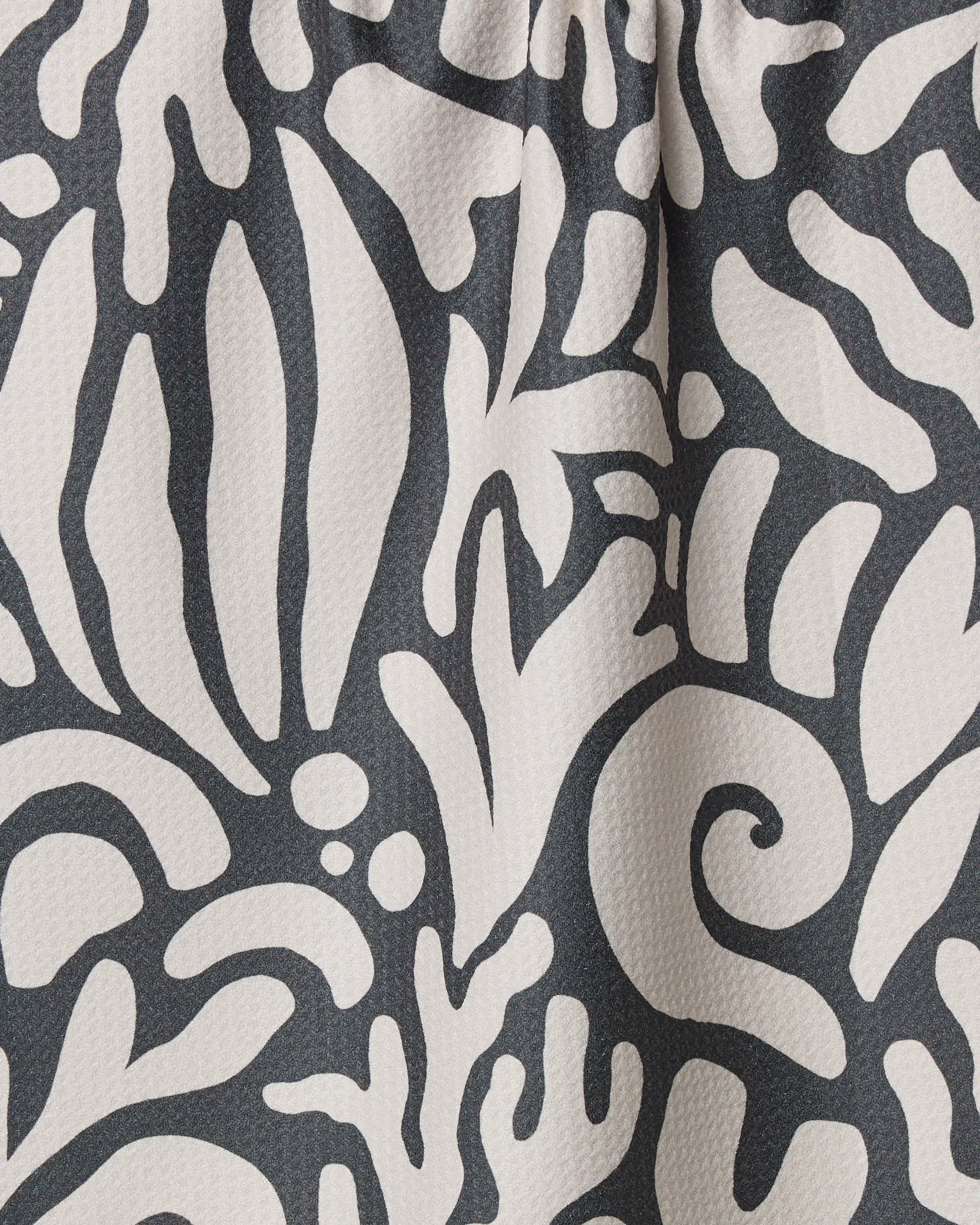 Close-up of Geometry's Inkwell Reef, a black tea towel with an abstract white pattern of organic swirls and leaves; ultra-absorbent, textured, slightly raised surface, and crafted from recycled materials.