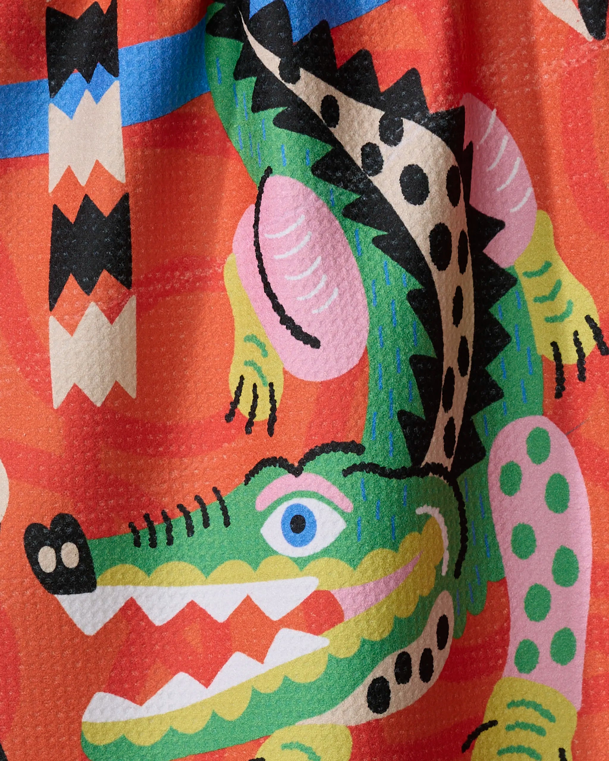 Jacaré by Camila Leão features a colorful, abstract crocodile with bold geometric patterns on an orange background—an eye-catching recycled kitchen or dish towel that adds flair and function to your space.