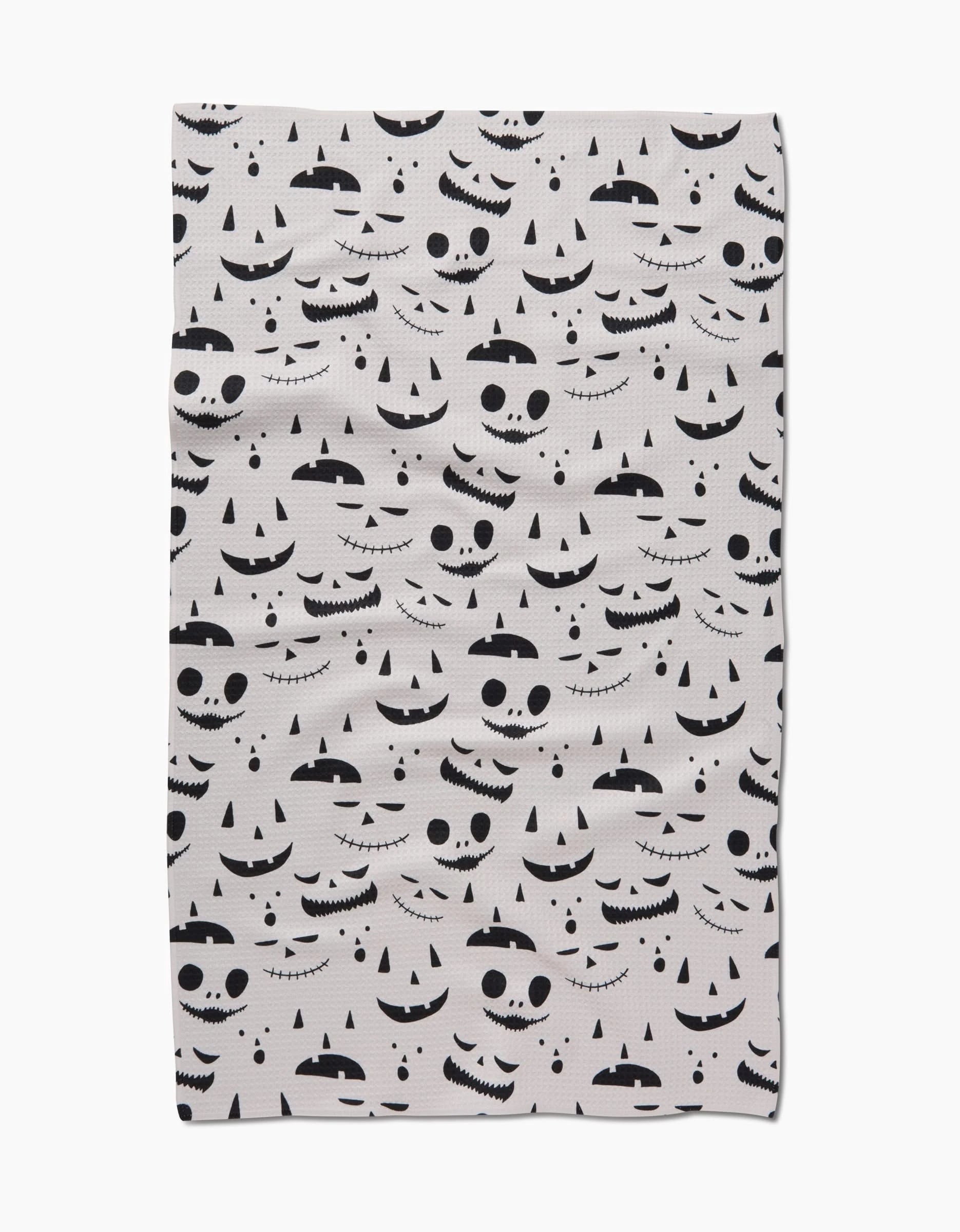 The Jack O Lantern Cream by Danelys Sidron is a white quick-drying towel decorated with black Halloween jack-o-lantern faces in various expressions scattered across the surface.